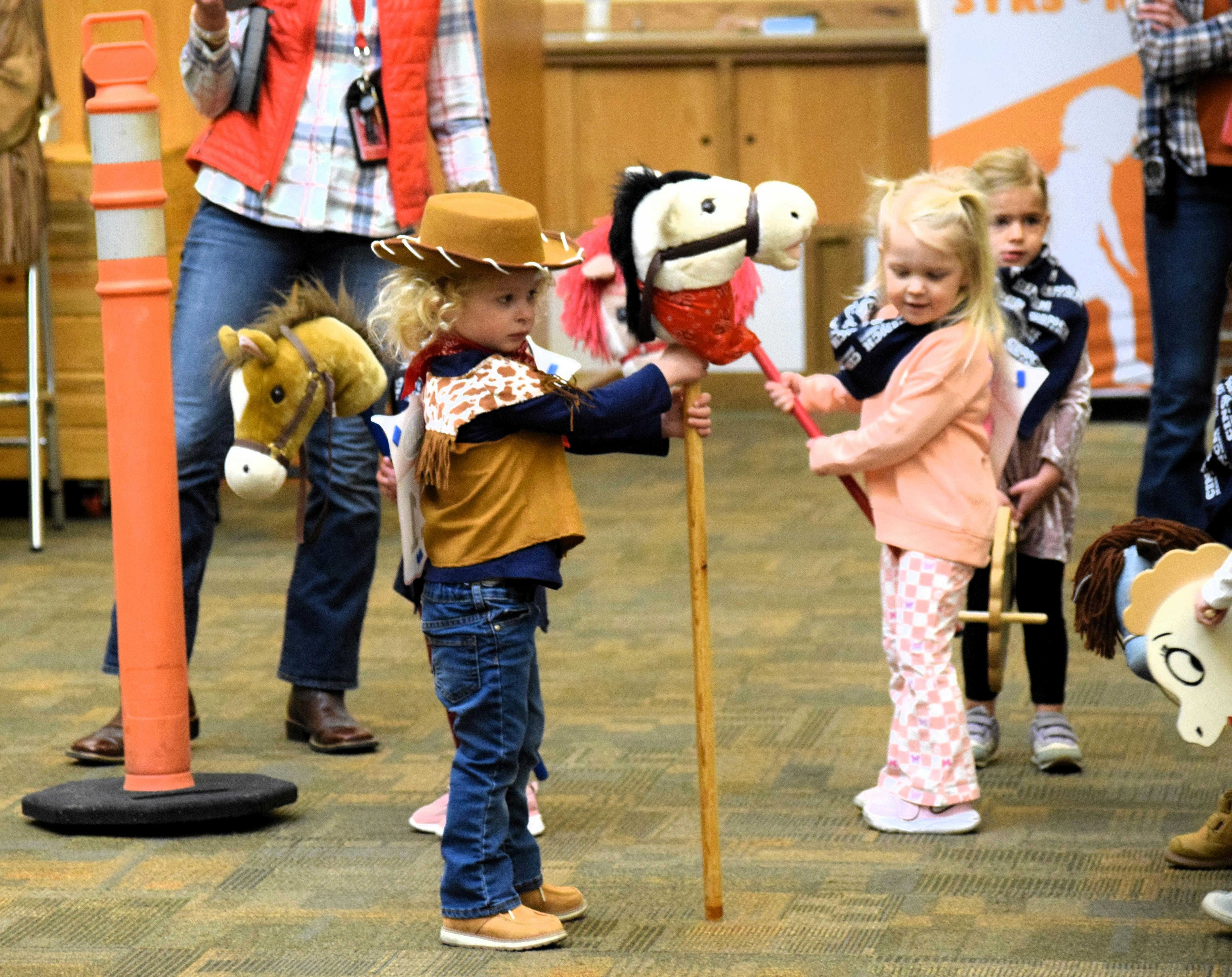 Child in cowboy hat holding a stick horse, another child holding a toy