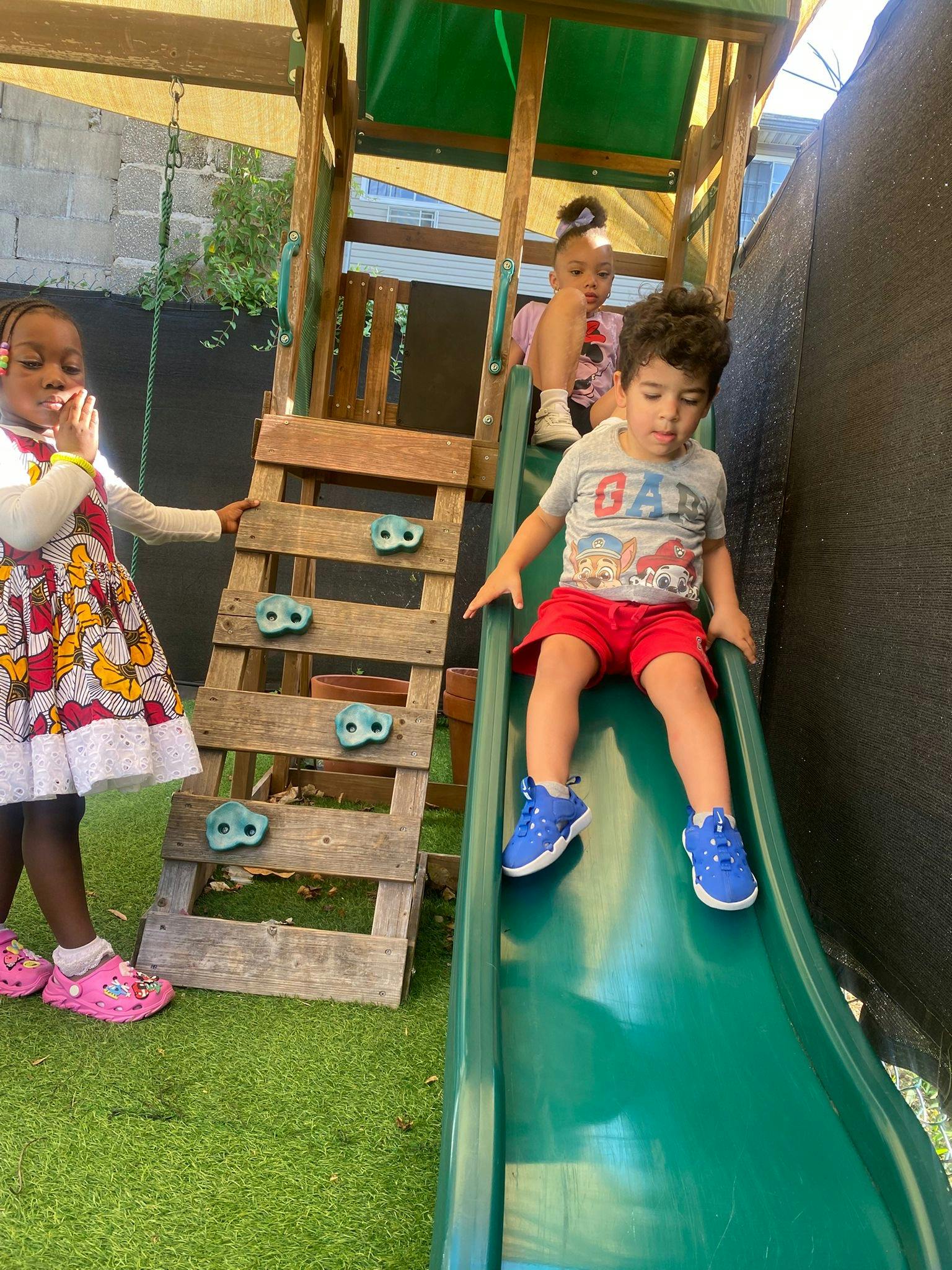 Three children on a playground structure, one sliding down