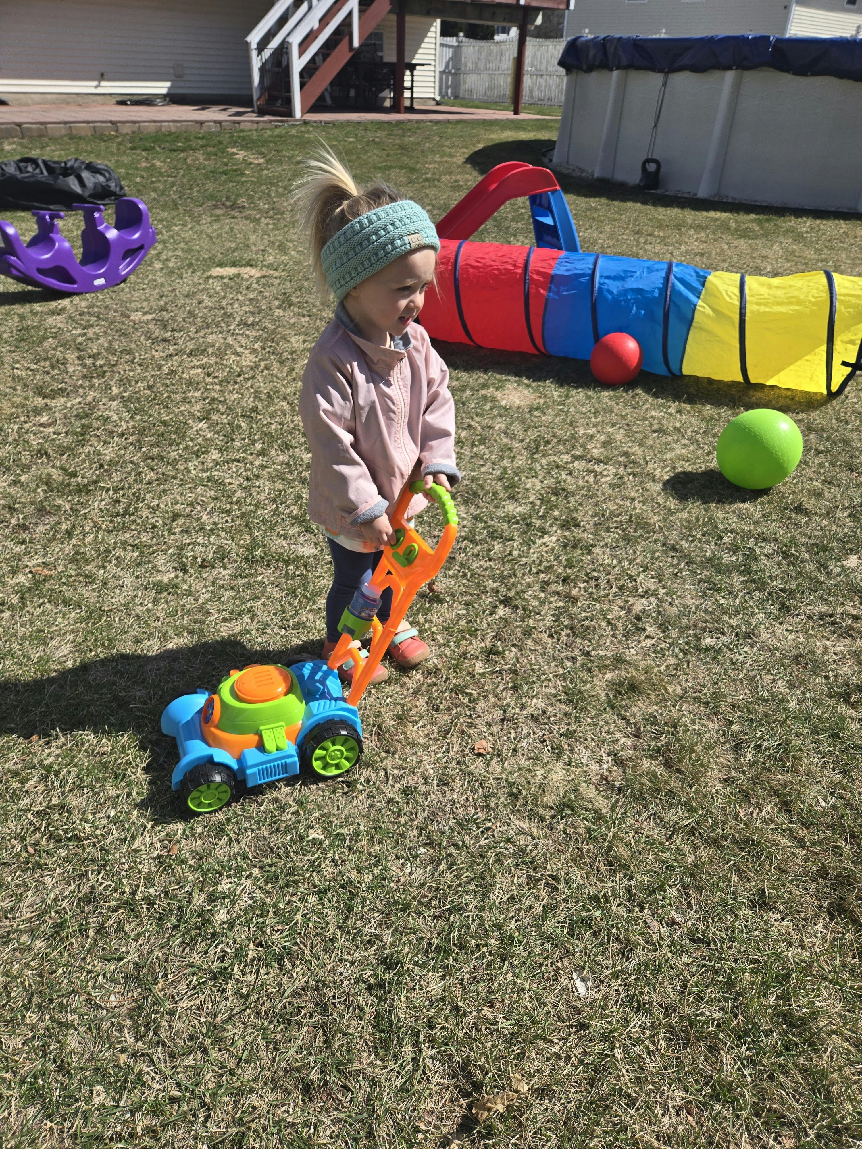 Child pushing a toy lawnmower on grass