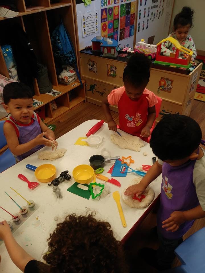 Children playing with dough and toys at a table in a classroom