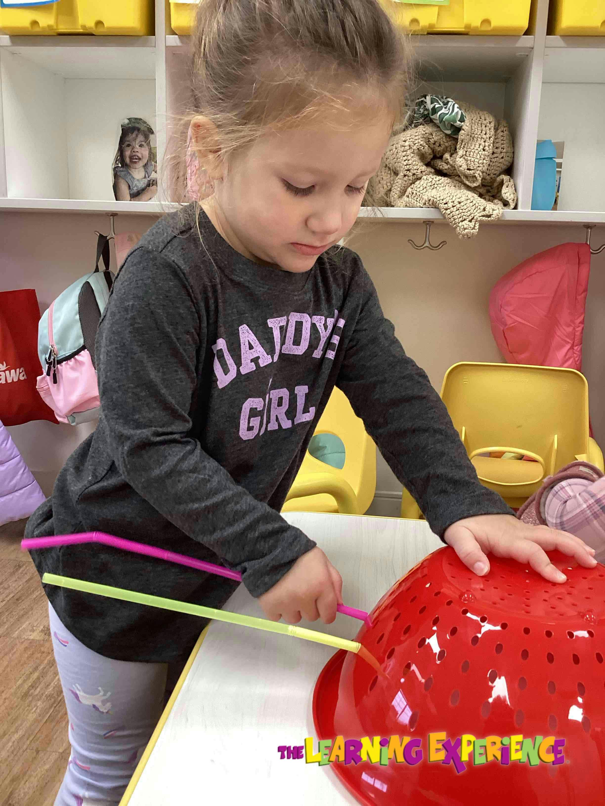 Child pushing straws into a red colander