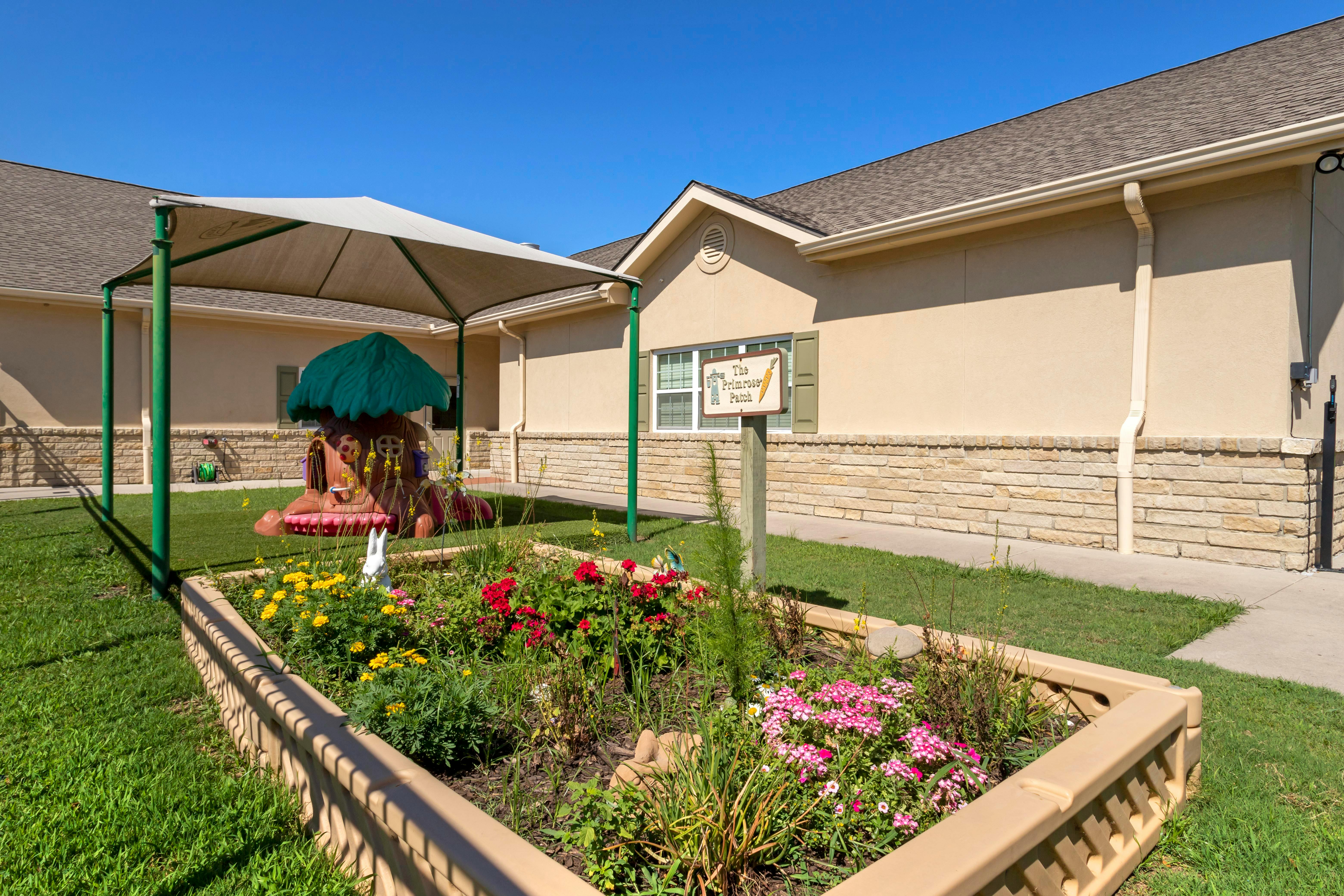 Flower bed in a grassy area with a building and covered play structure in the background