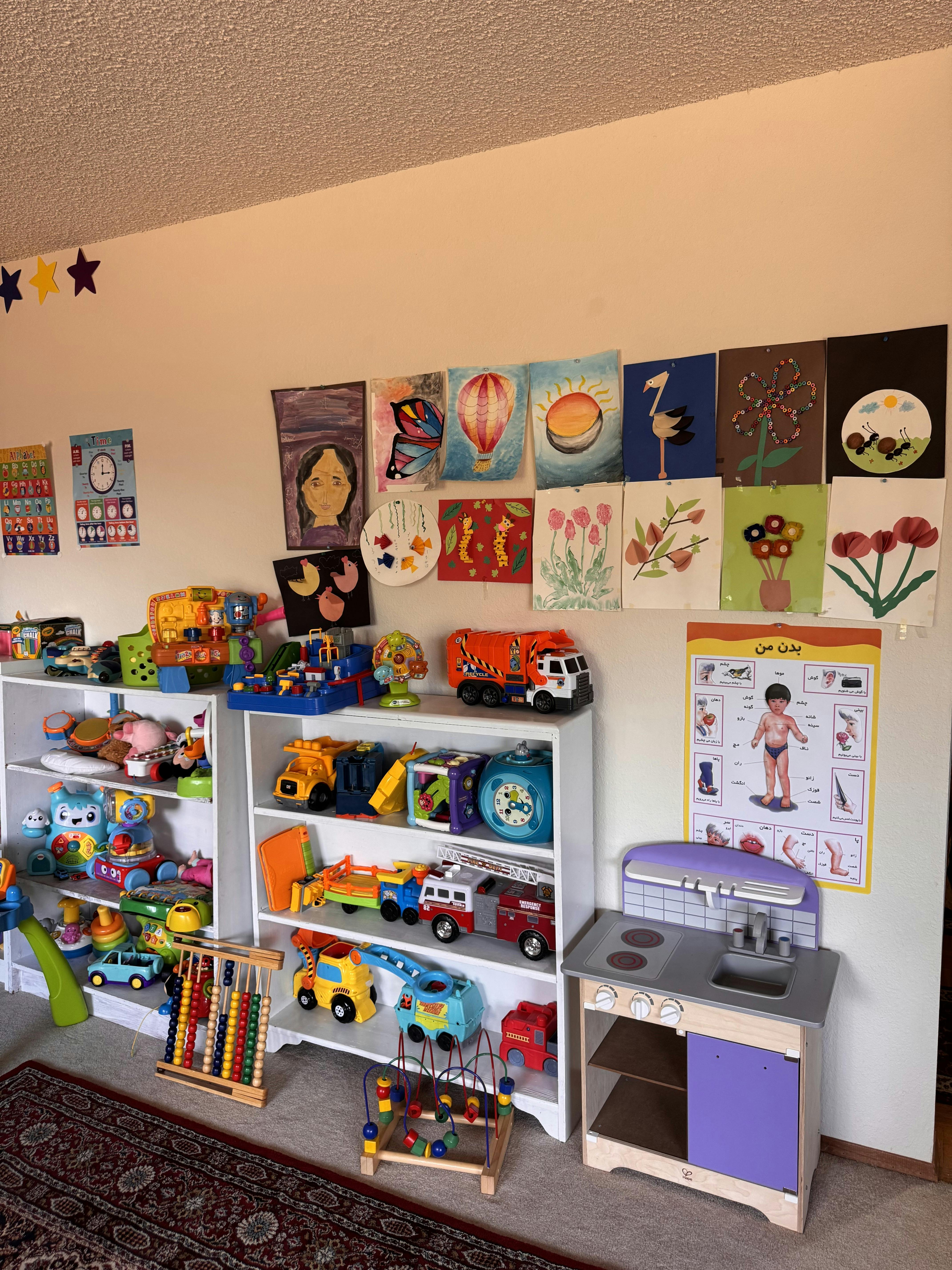 Playroom with shelves of toys, children's artwork on the wall, and a play kitchen