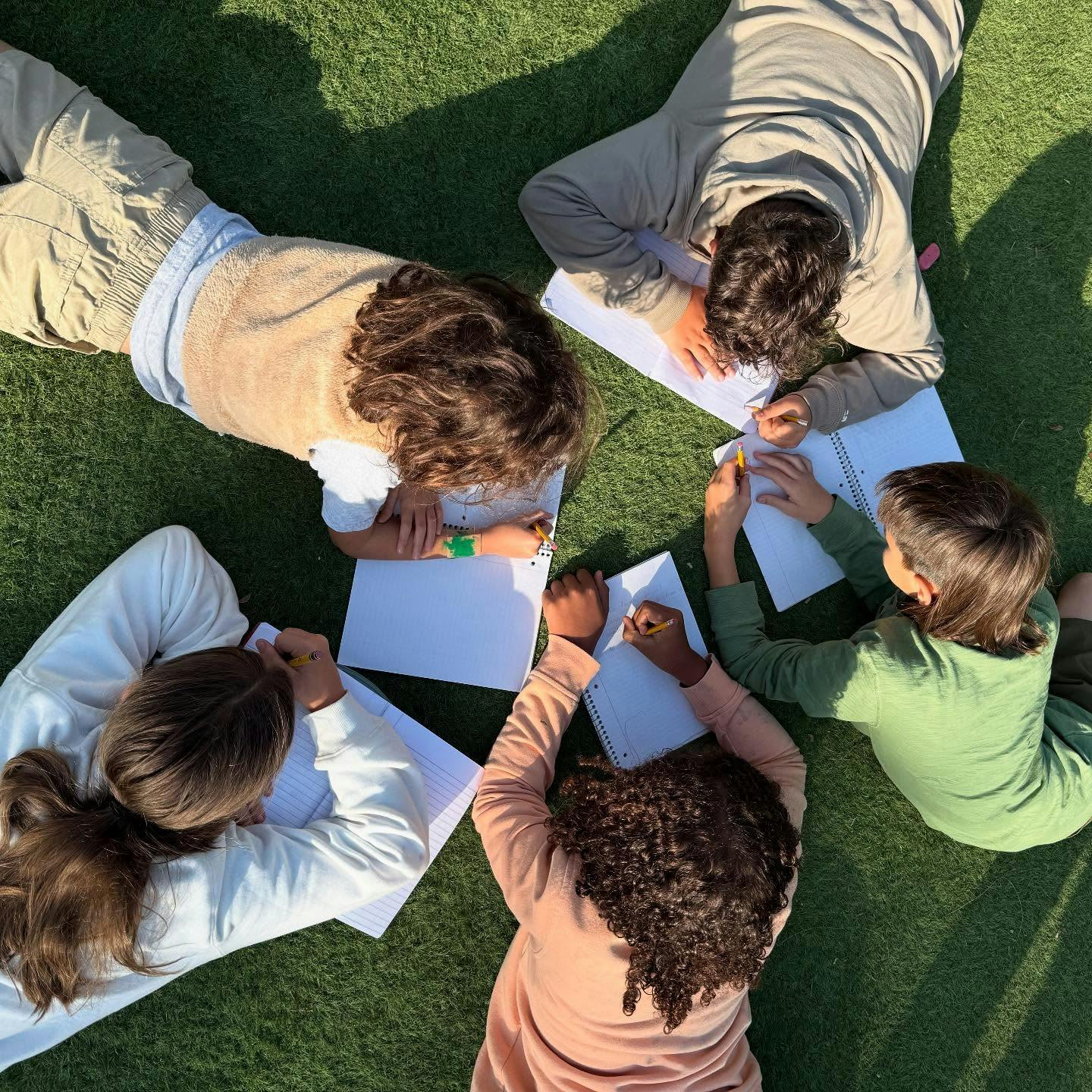 Children lying on grass drawing on paper
