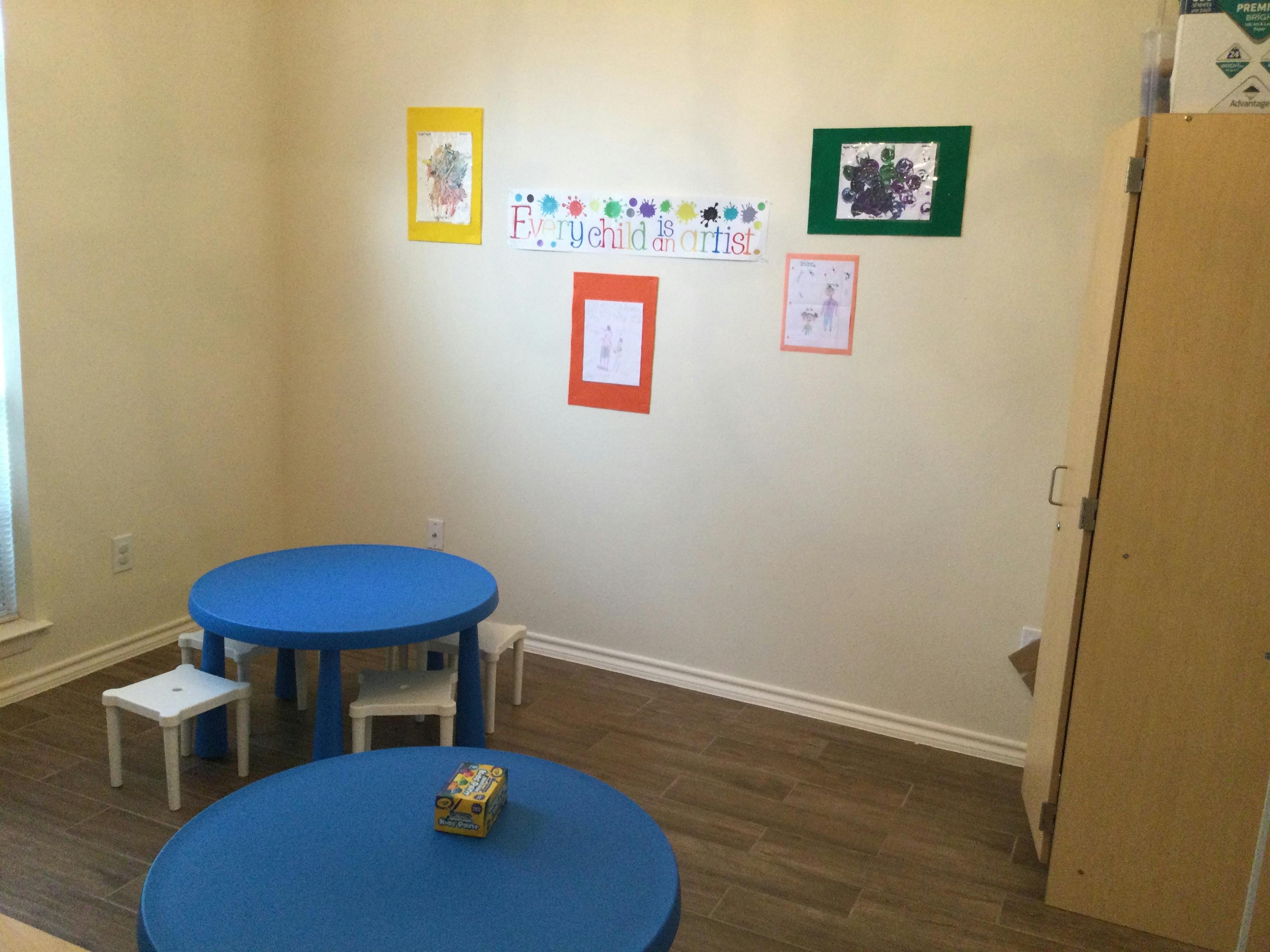 Two blue tables with small chairs in a room with drawings on the wall