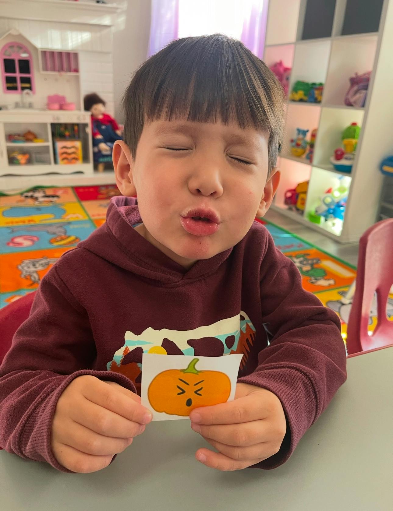 Child with eyes closed holding a pumpkin sticker