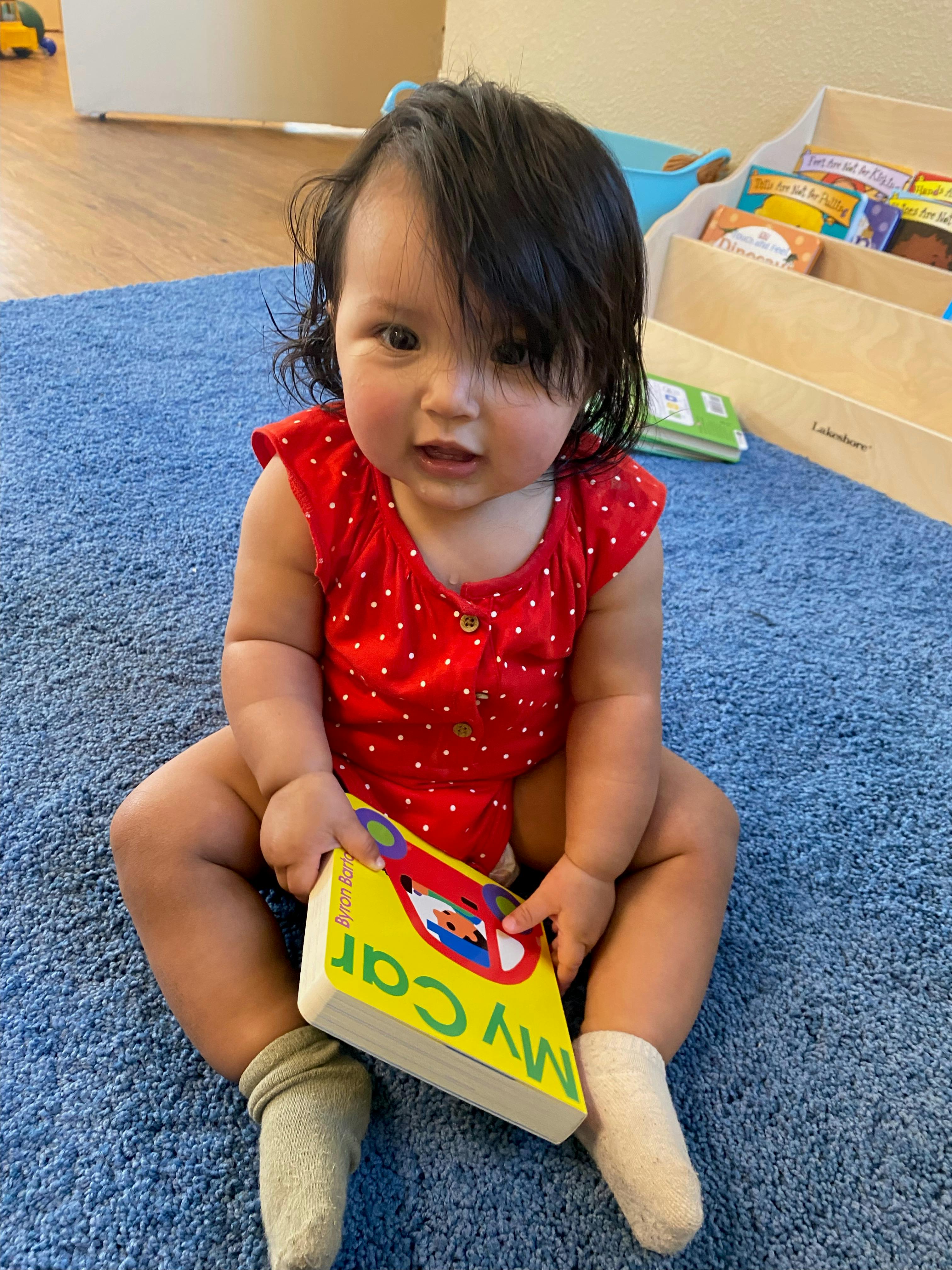 Child sitting on a blue rug holding a book titled "My Car"