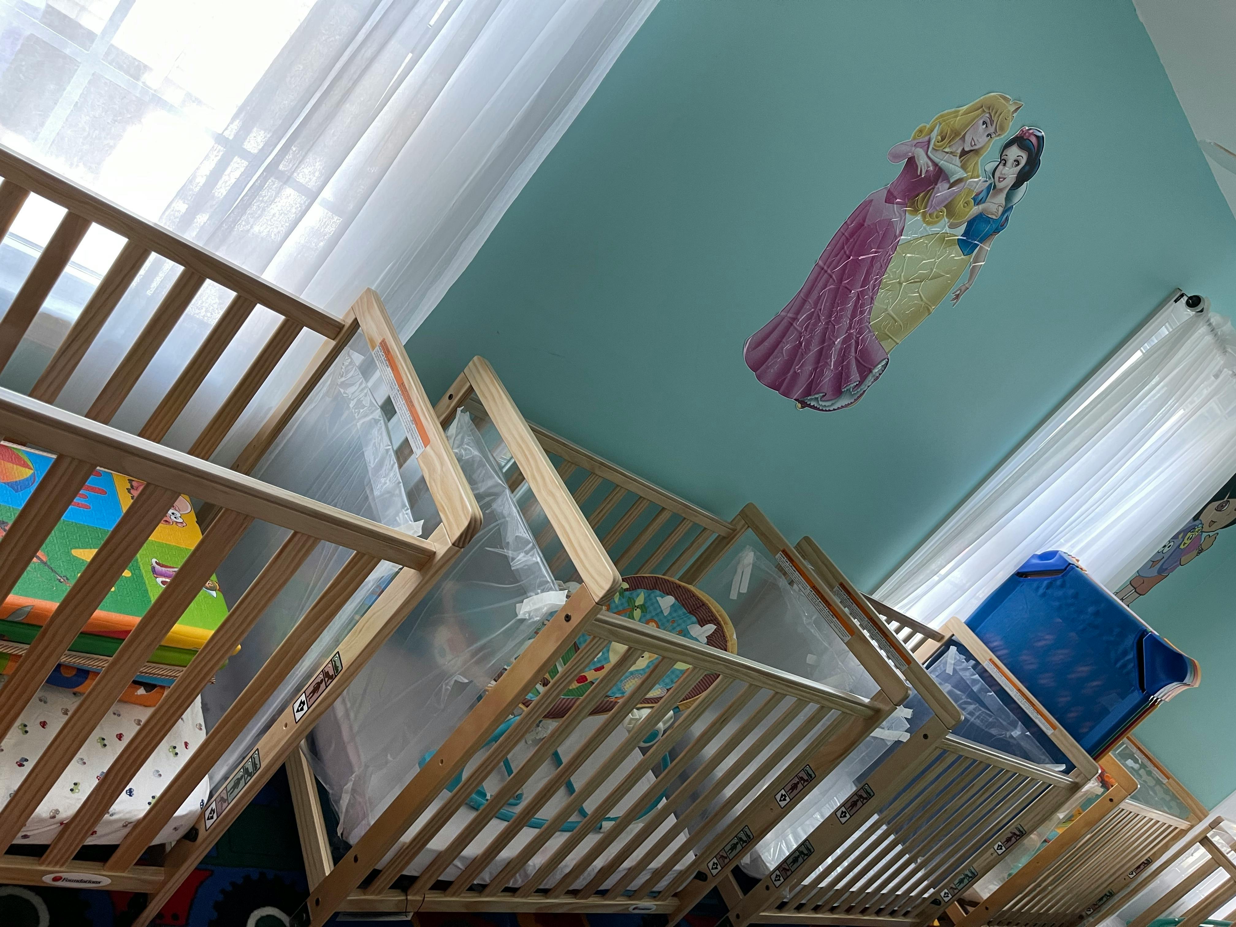 Multiple wooden cribs in a room with a princess decal on the ceiling