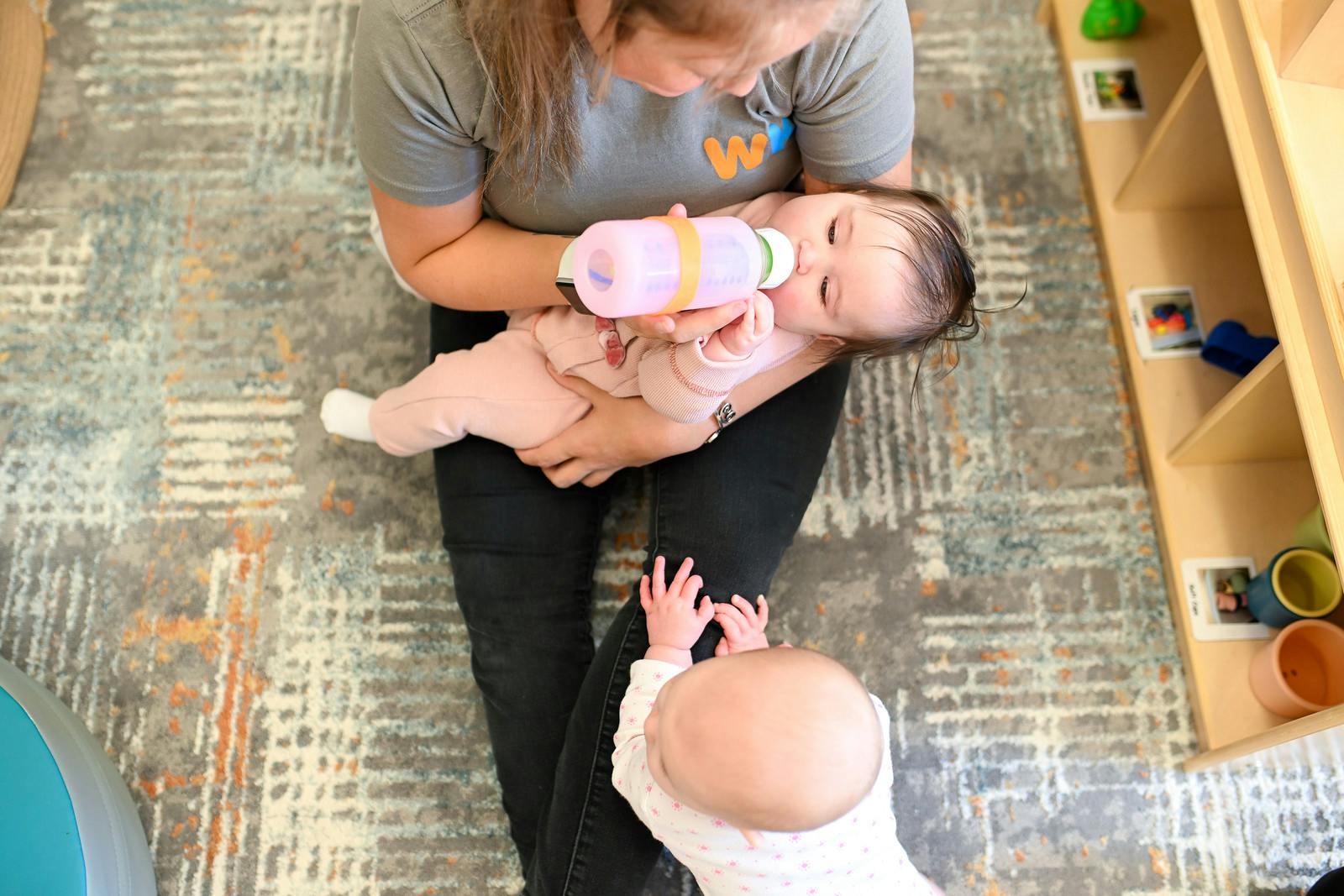 Person holding and bottle-feeding an infant, another infant nearby