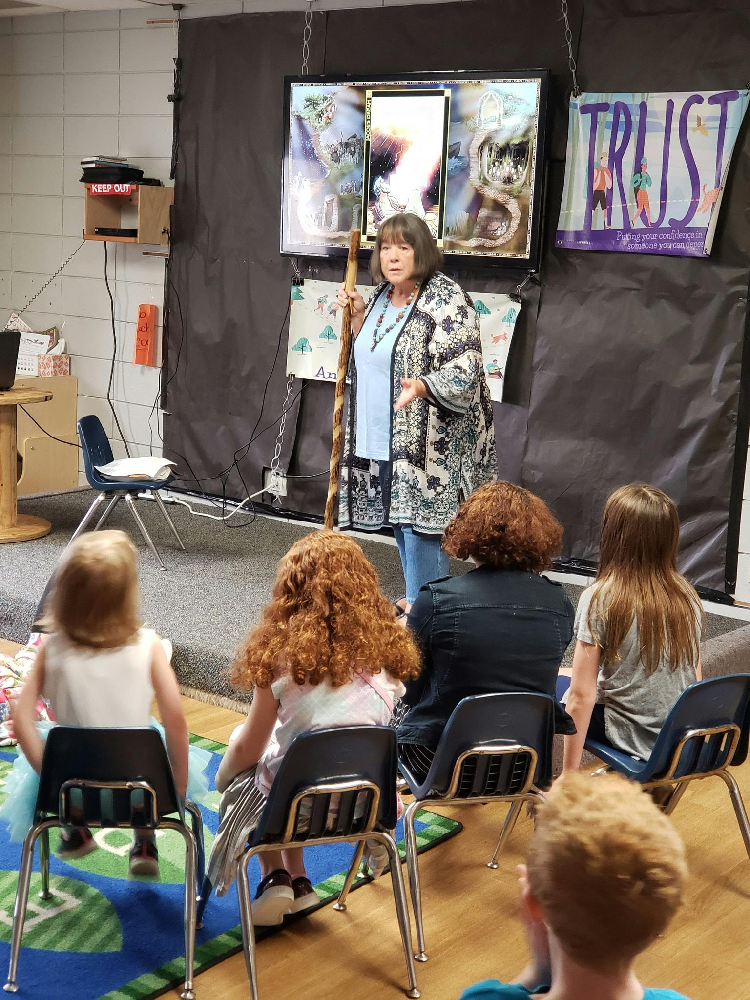Person speaking to a group of children and adults in a classroom
