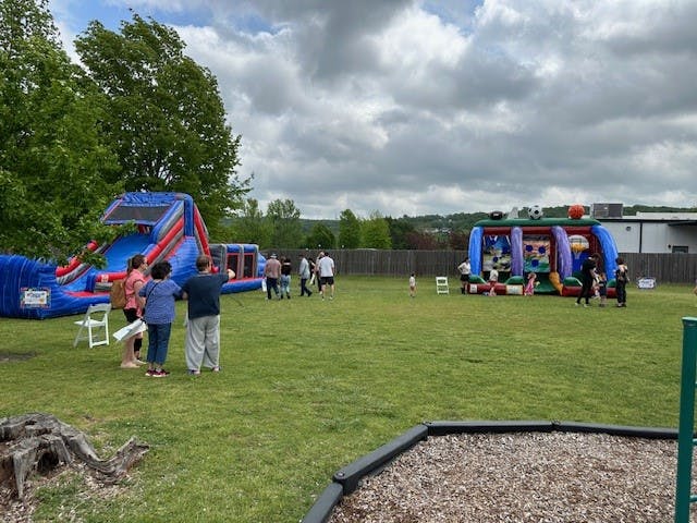 People gathered on a grassy field with inflatable slides and bounce houses