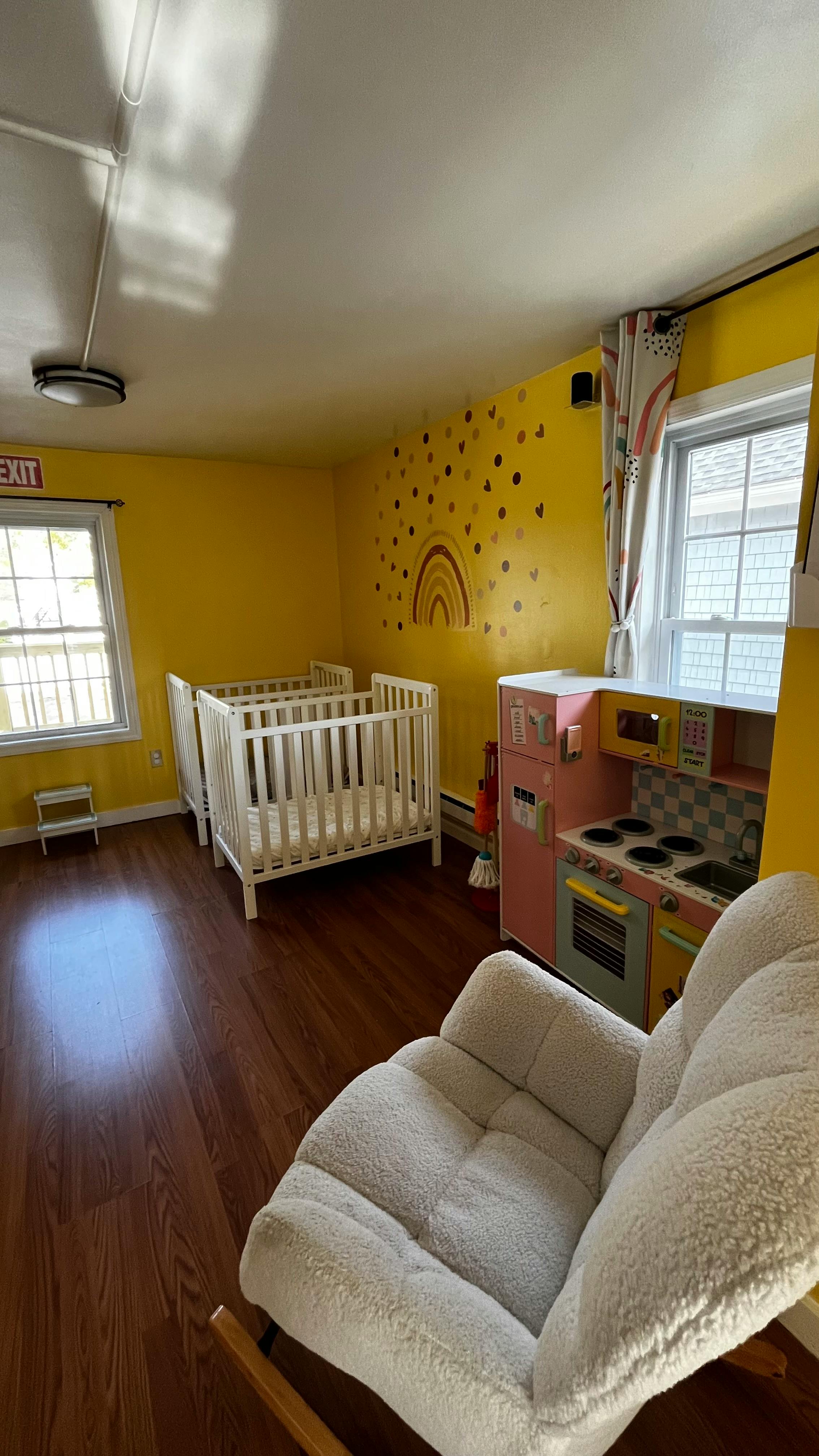 Two cribs and a toy kitchen in a room with yellow walls