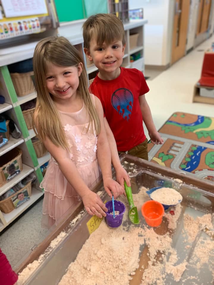 Two children playing in a sand table with toys
