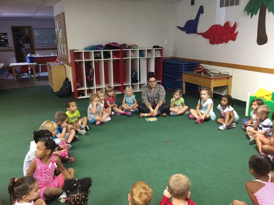 Adult and children sitting in a circle on a green carpet