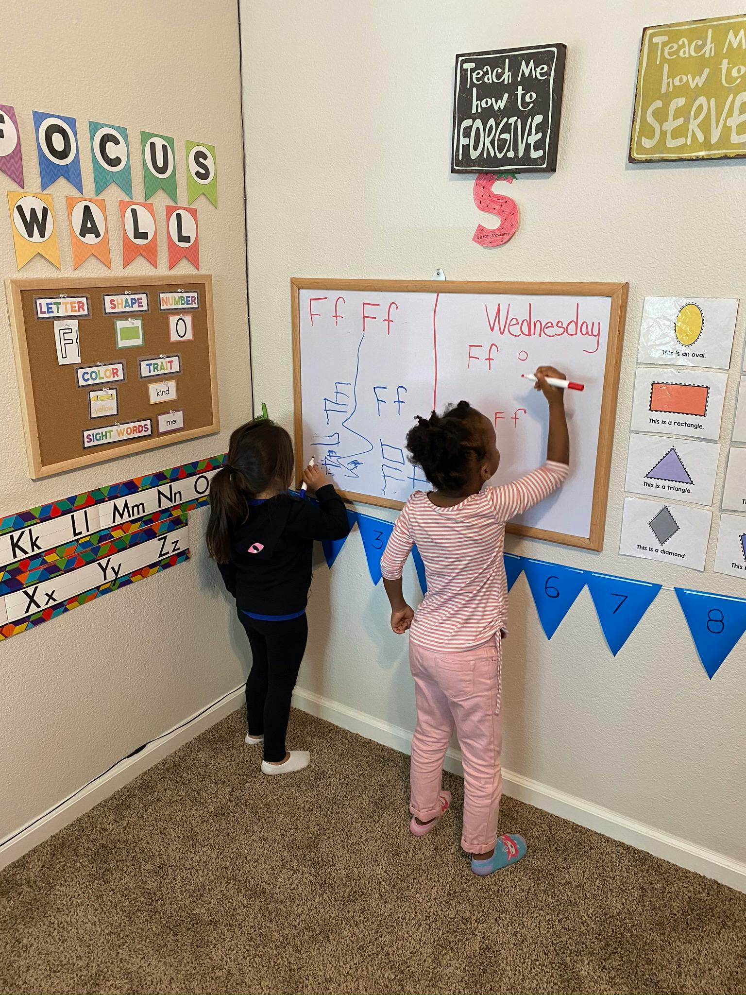 Two children writing on a whiteboard in a classroom
