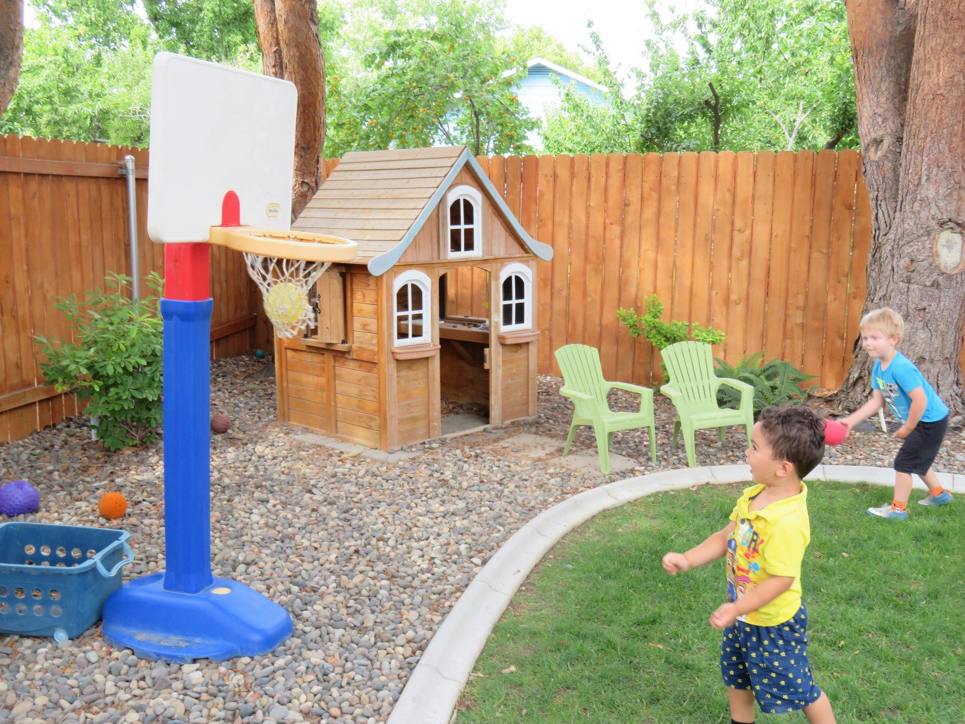 Two children playing with a ball in a backyard with a playhouse and basketball hoop