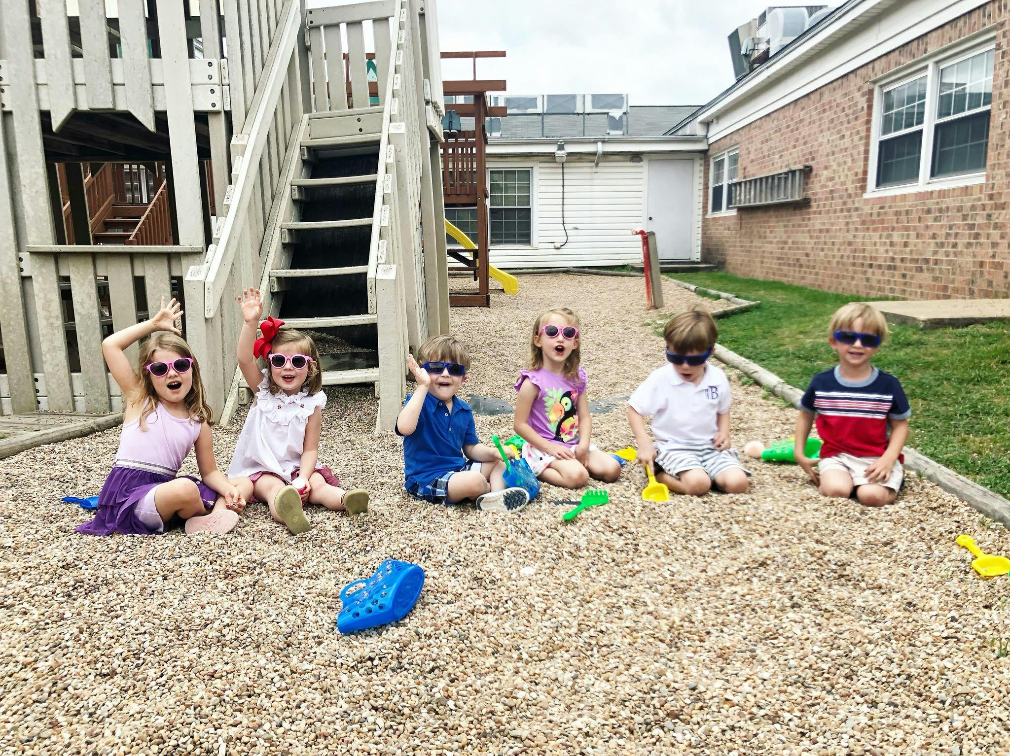 Six children wearing sunglasses sitting on wood chips on a playground
