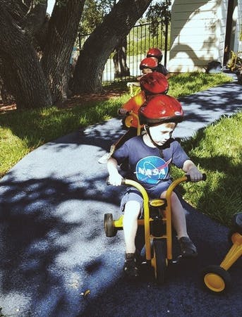 Children in red helmets riding tricycles in a line outdoors