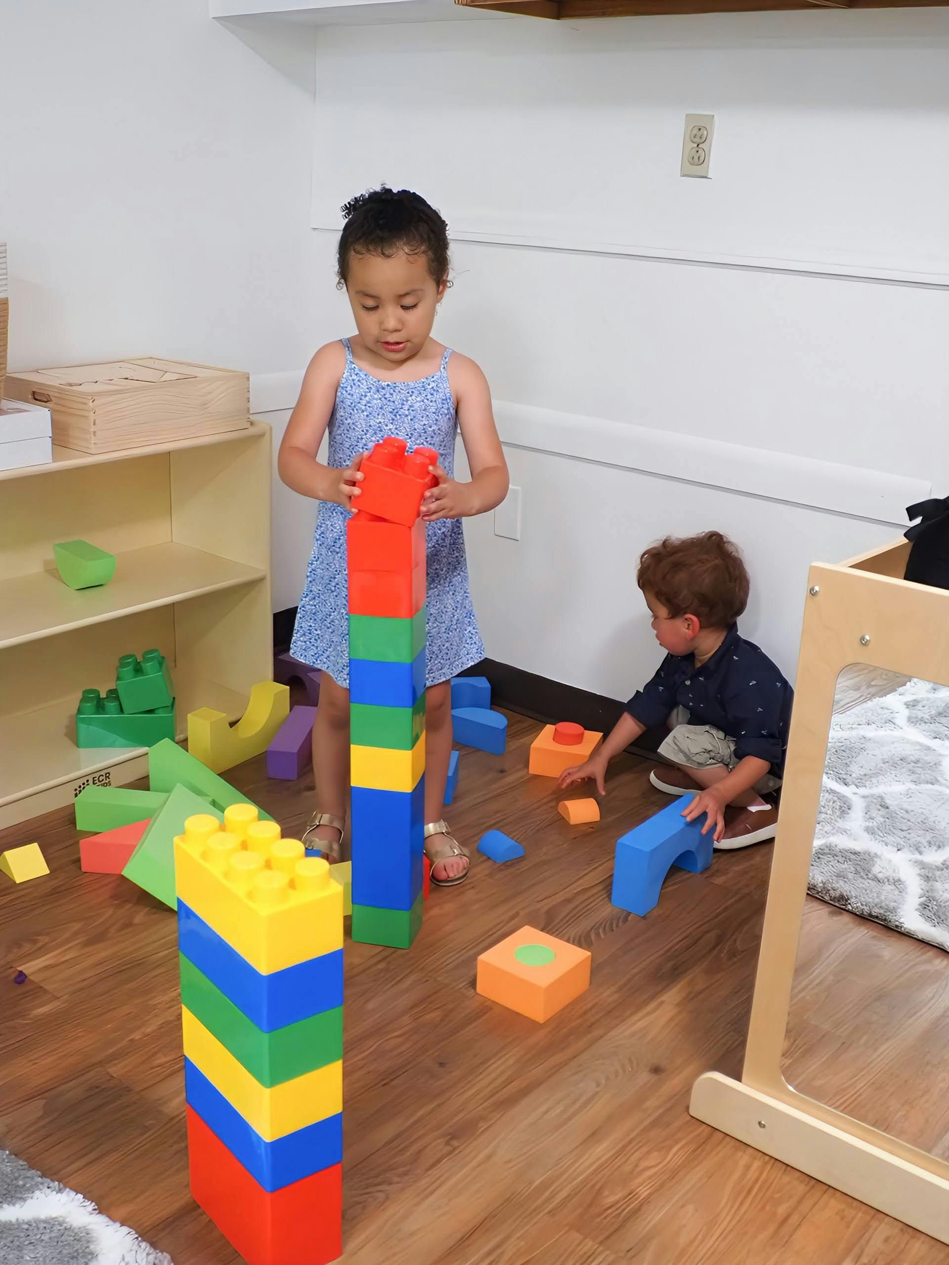 Child building a tall block tower, another child playing with blocks on the floor