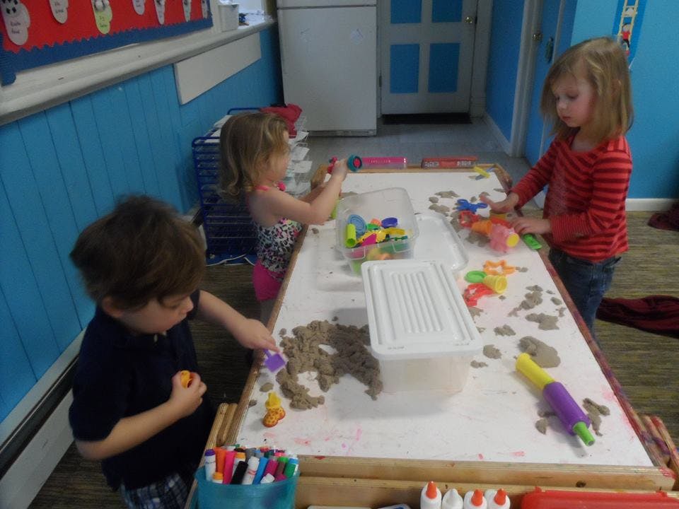 Three children playing with sand and toys at a table