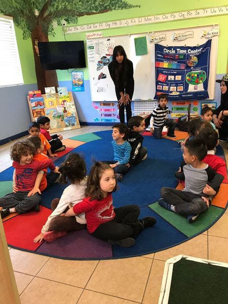 Adult and children sitting on a colorful rug in a classroom