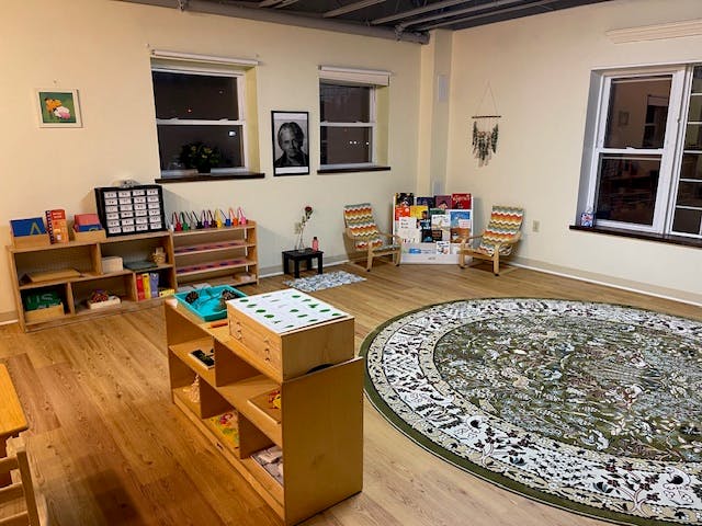 Classroom with wooden shelves, a round rug, and small chairs