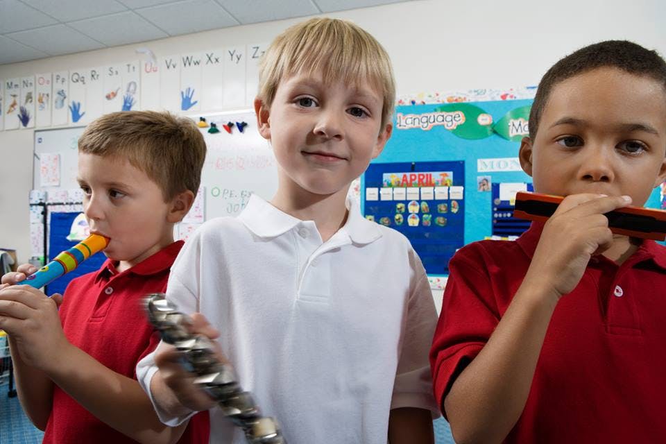 Three children playing musical instruments in a classroom
