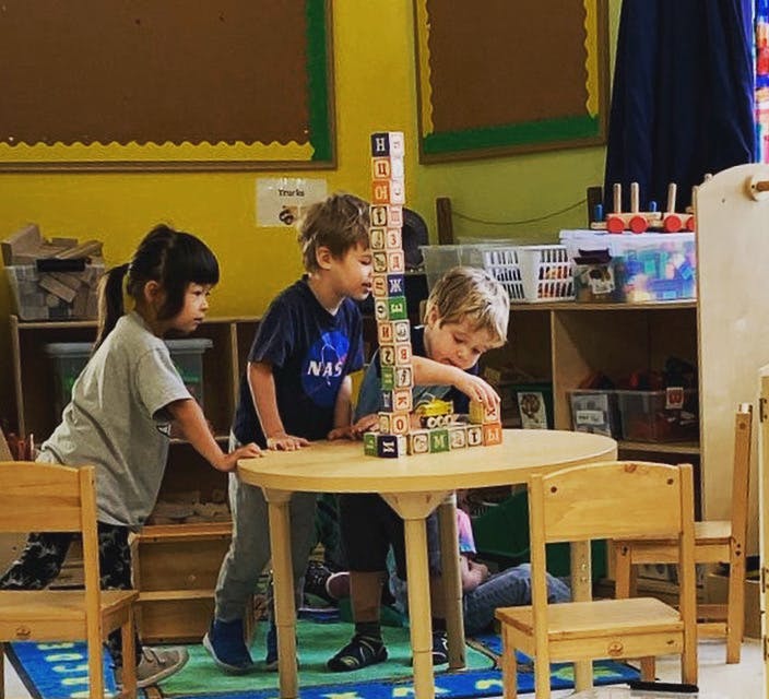 Three children building a tall tower with blocks on a table in a classroom