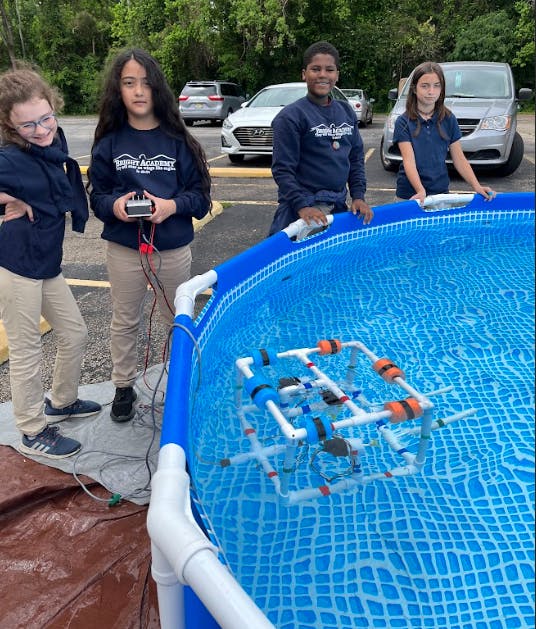 Three teens and a child with a remote-controlled underwater robot in a pool