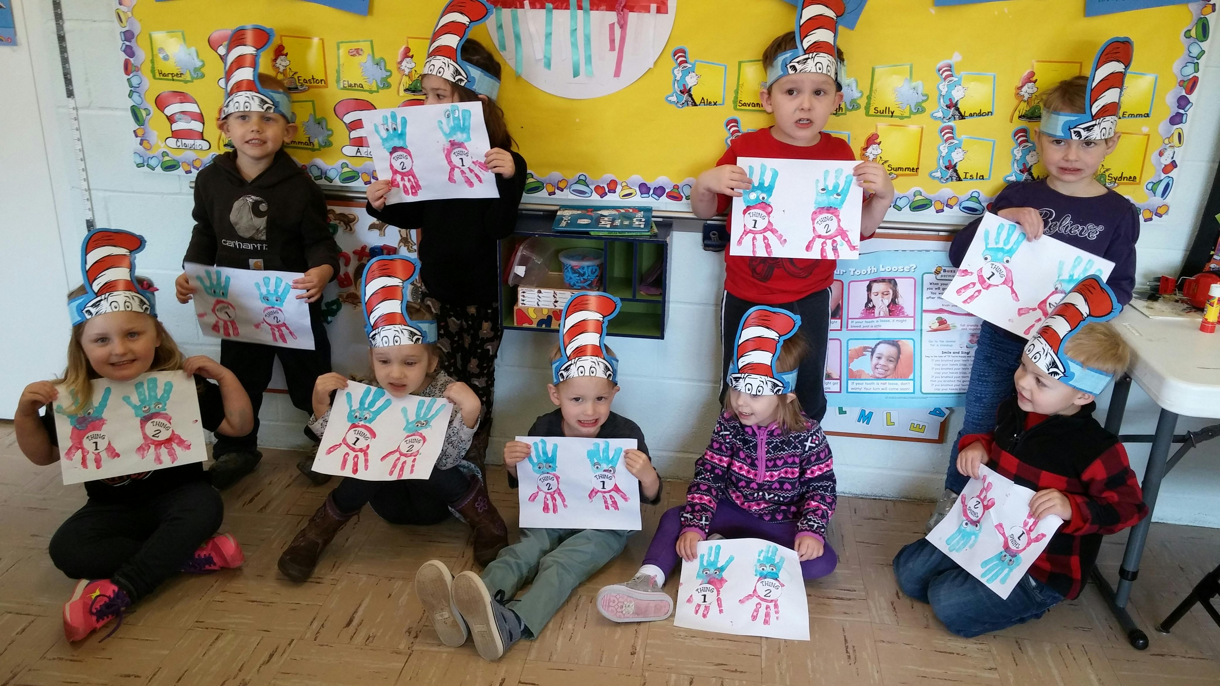 Children wearing striped hats and holding up artwork in-progress artwork