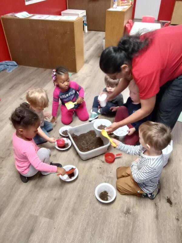 Adult and children playing with dirt and small shovels on the floor