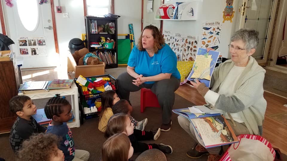 Two people reading to a group of children in a classroom