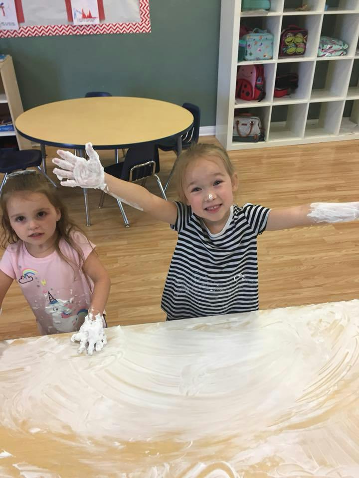 Two children playing with white foam on a table in a classroom