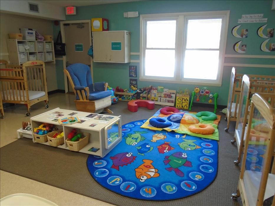 A colorful room with multiple cribs, a blue rocking chair, and a play mat