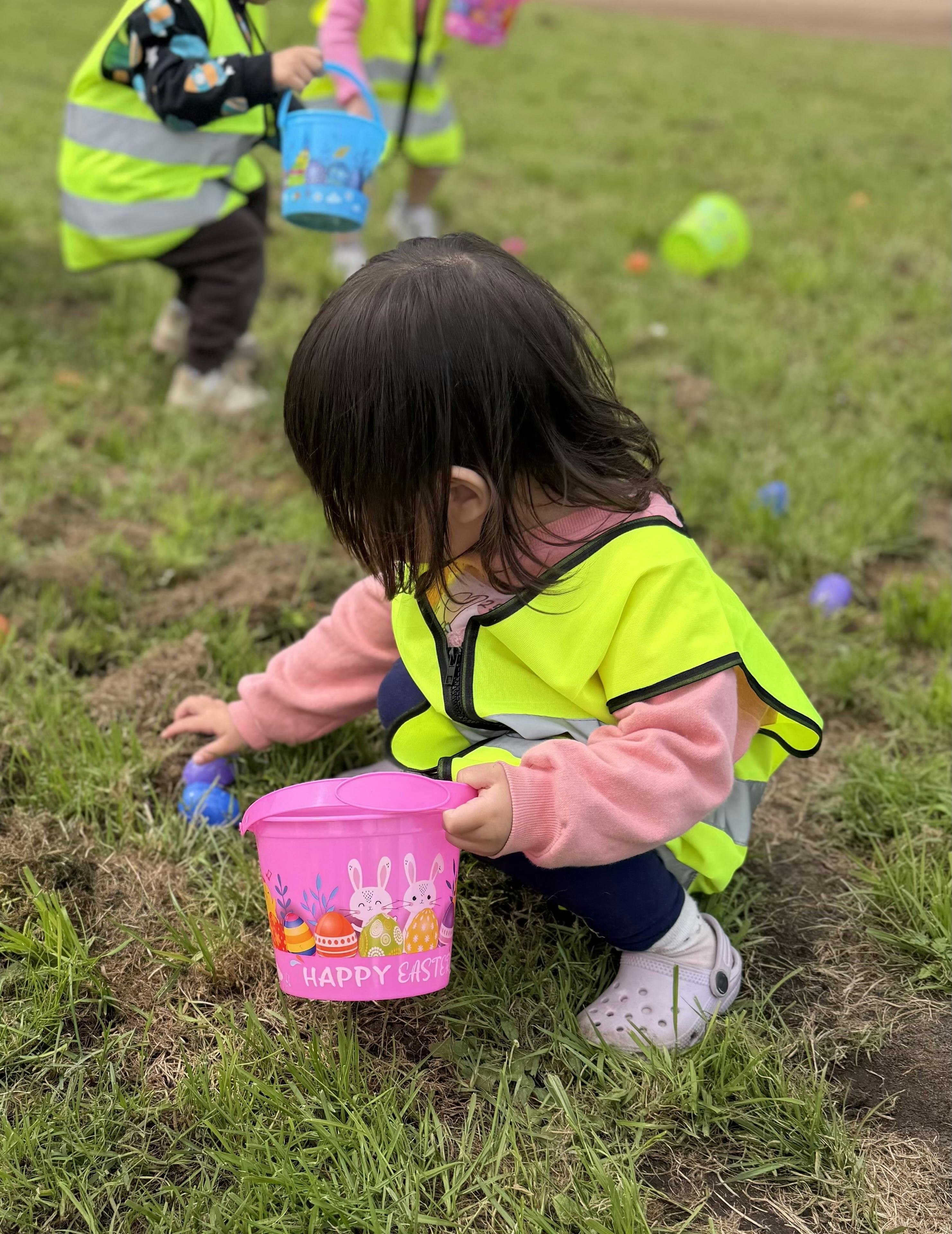 Child in a high-visibility vest picking up plastic eggs on a grass field