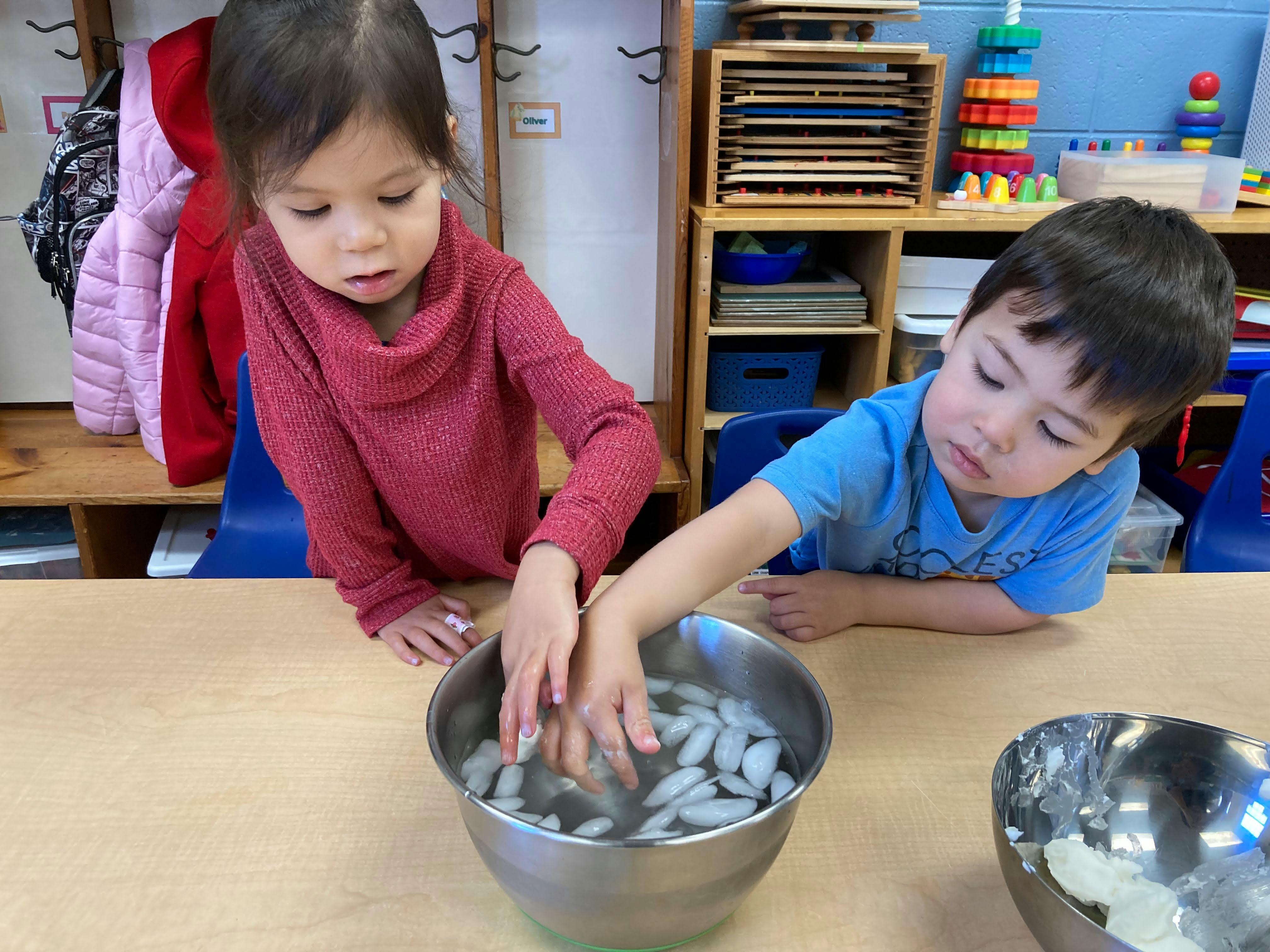 Two children with hands in bowls of ice water in a classroom