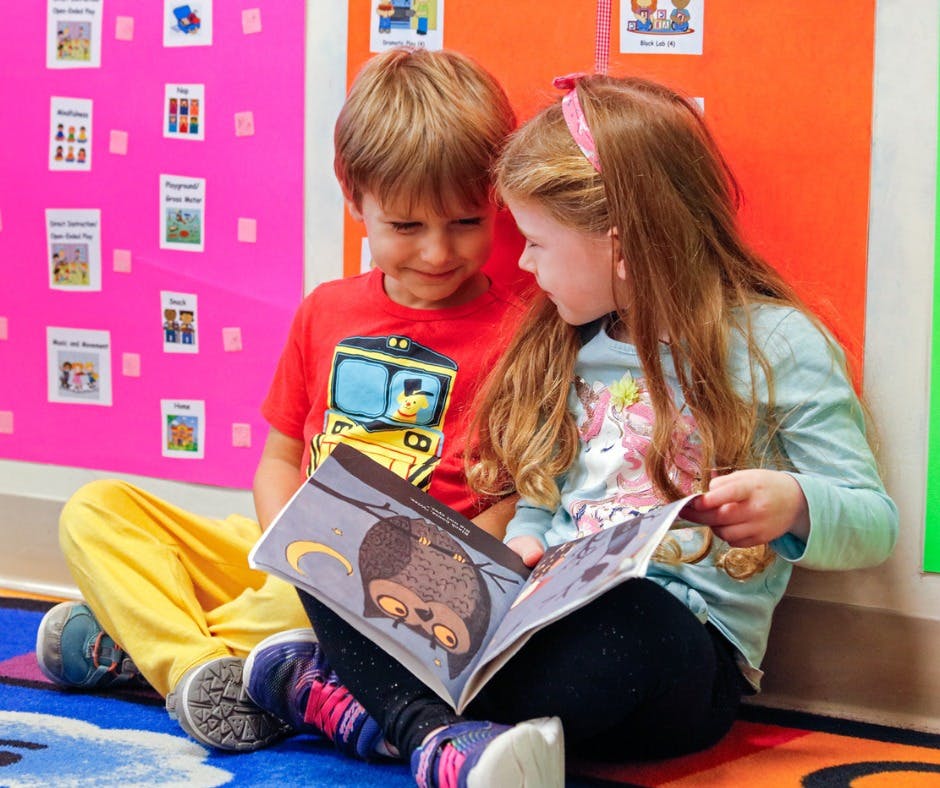 Two children sitting on the floor reading a book together