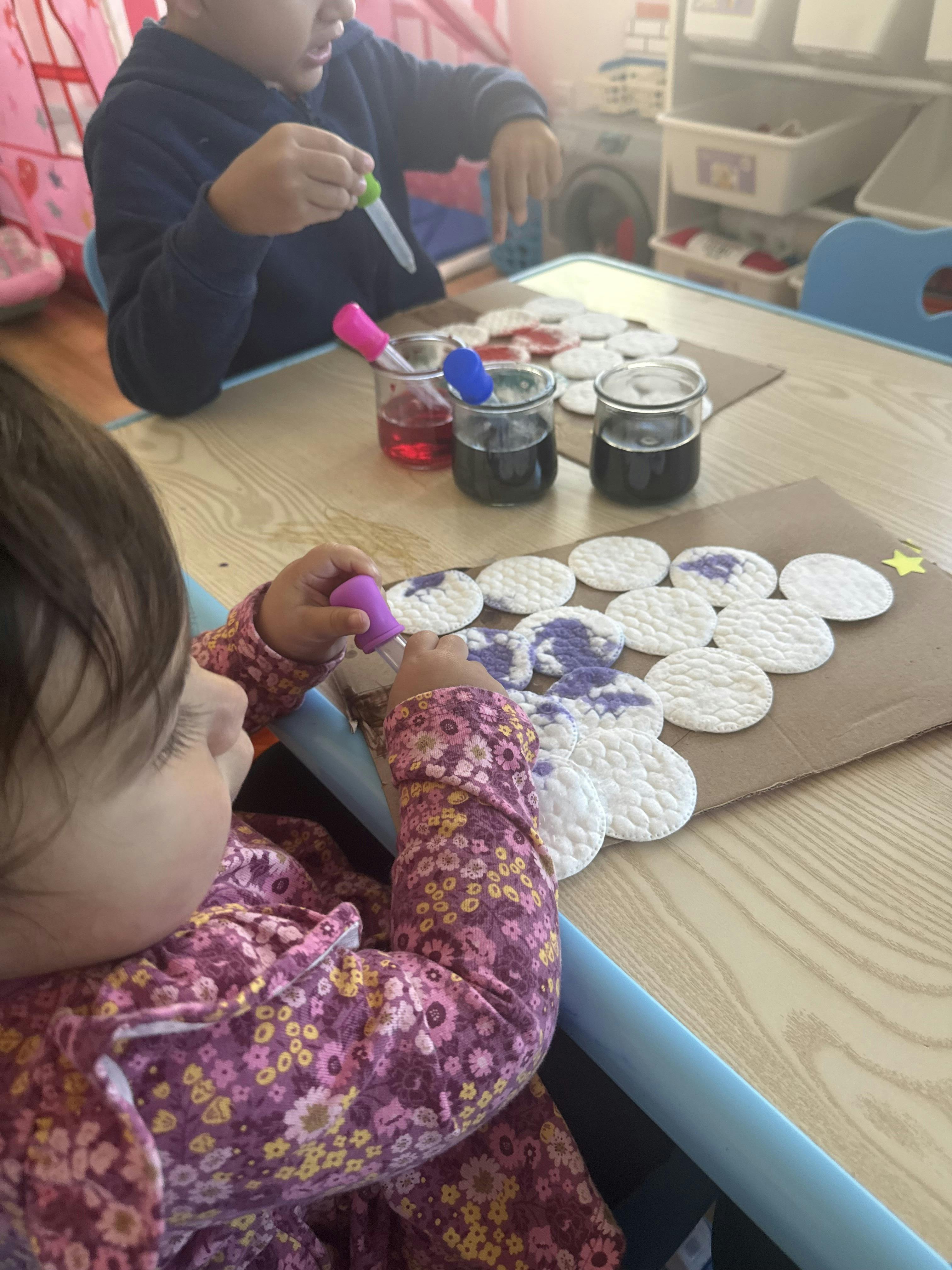 Two children doing an art activity with cotton pads and colored liquids