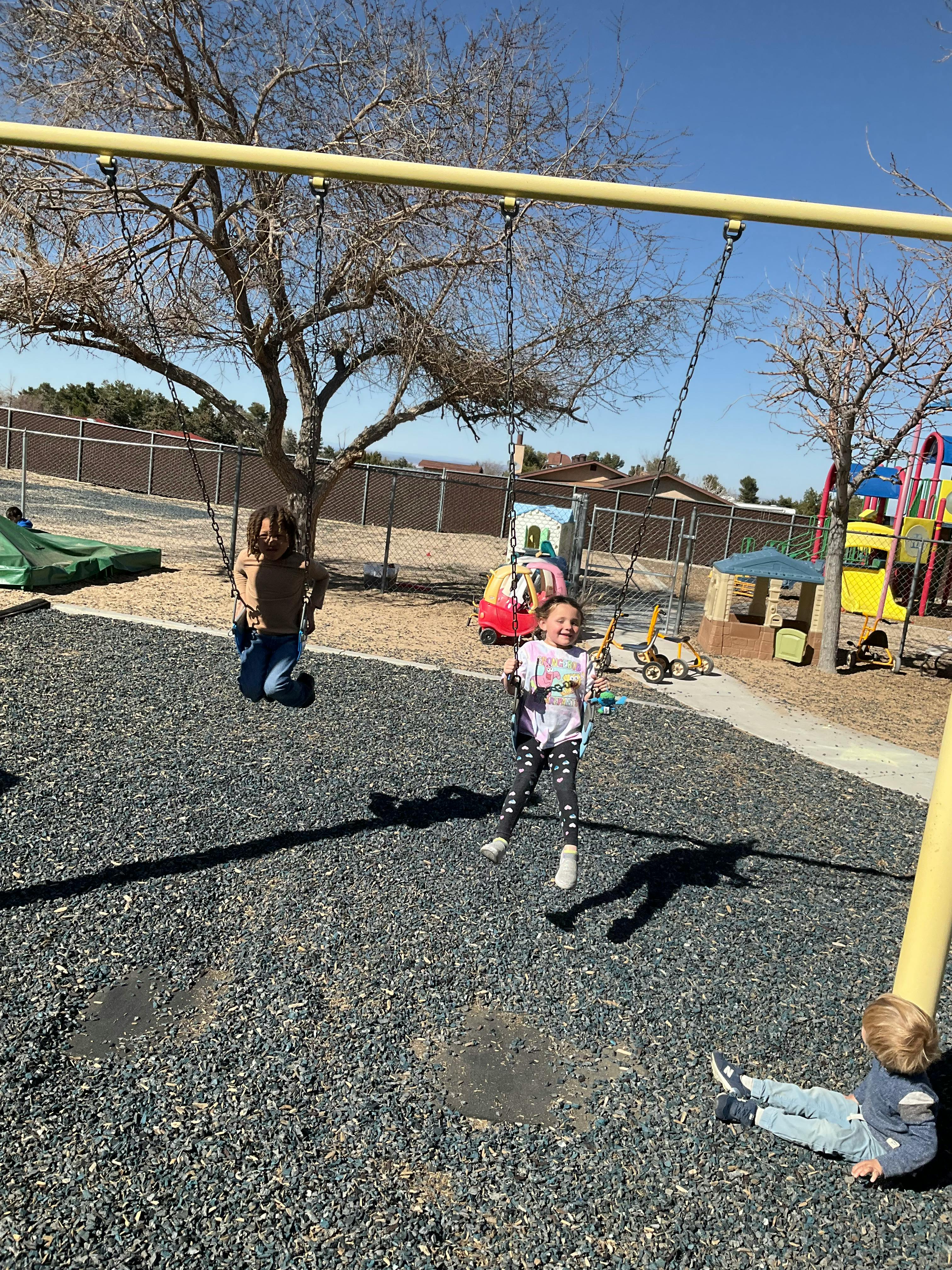 Three children playing on a swing set at a playground