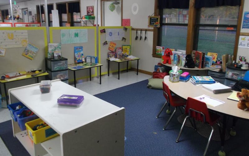 A colorful classroom with child-sized tables, chairs, and shelves filled with books and toys