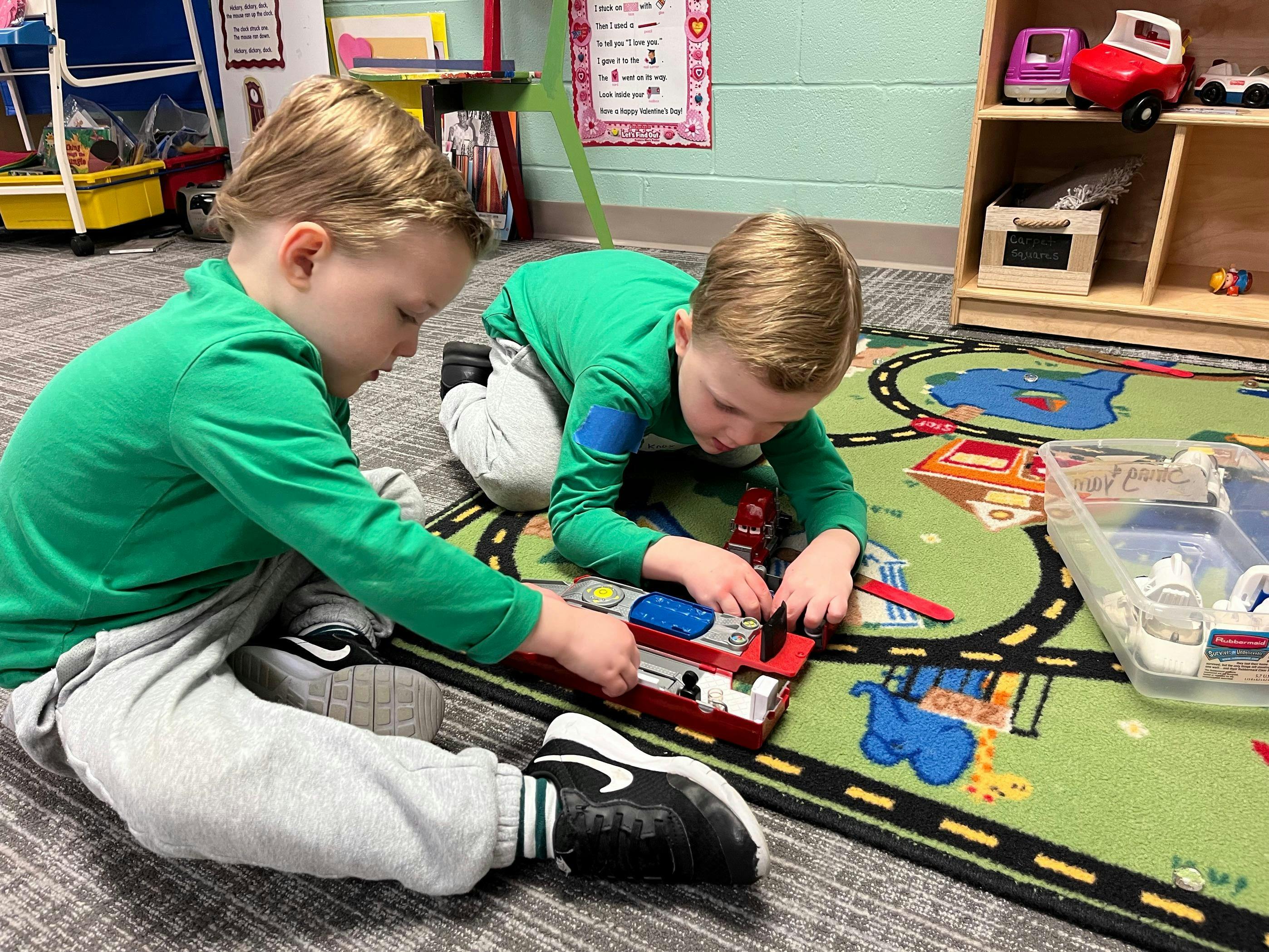 Two children playing with a toy on a rug in a classroom
