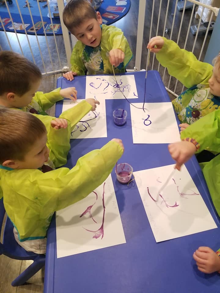Children in smocks painting at a table