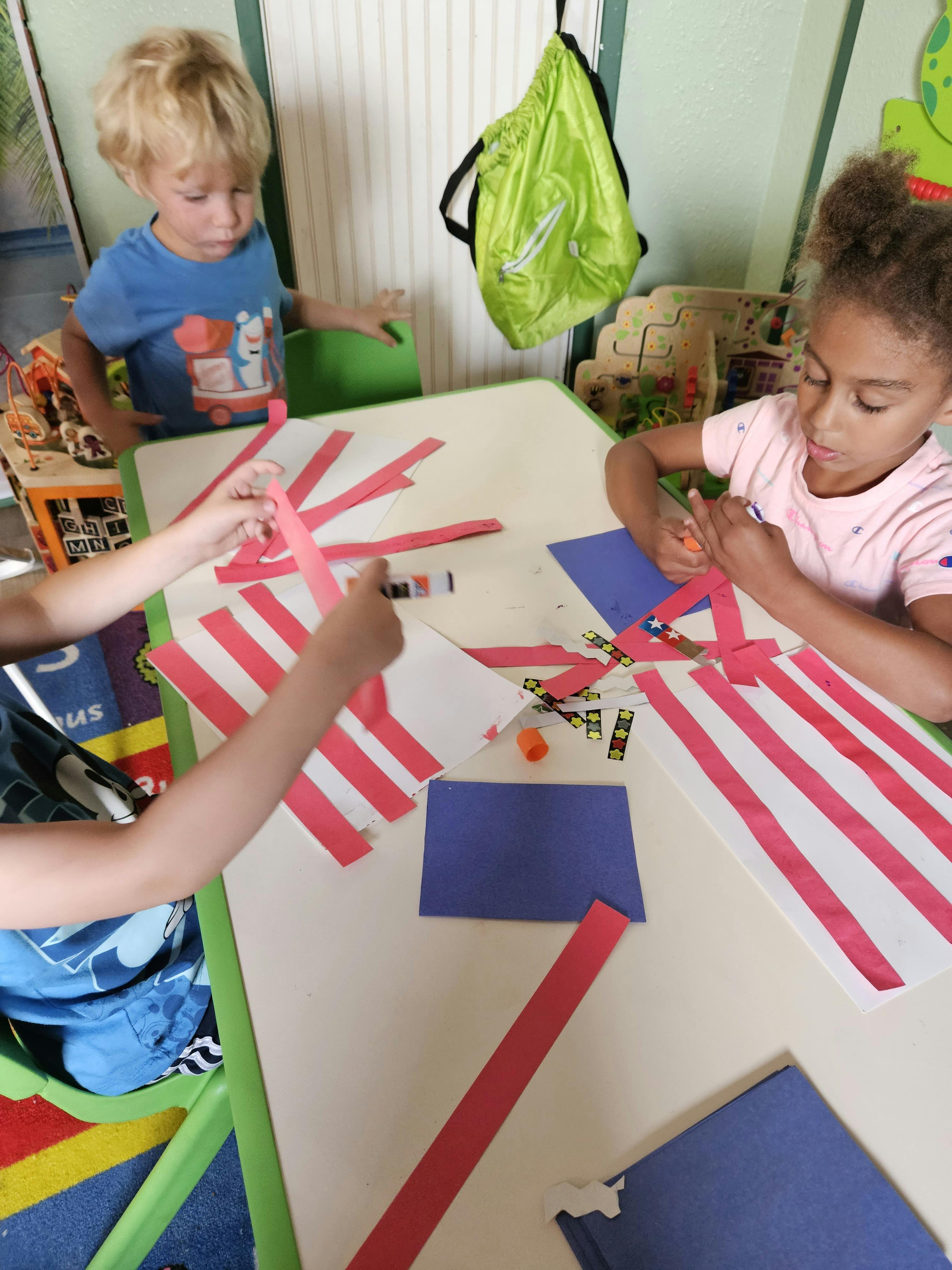 Children making crafts with red and white paper strips and blue paper