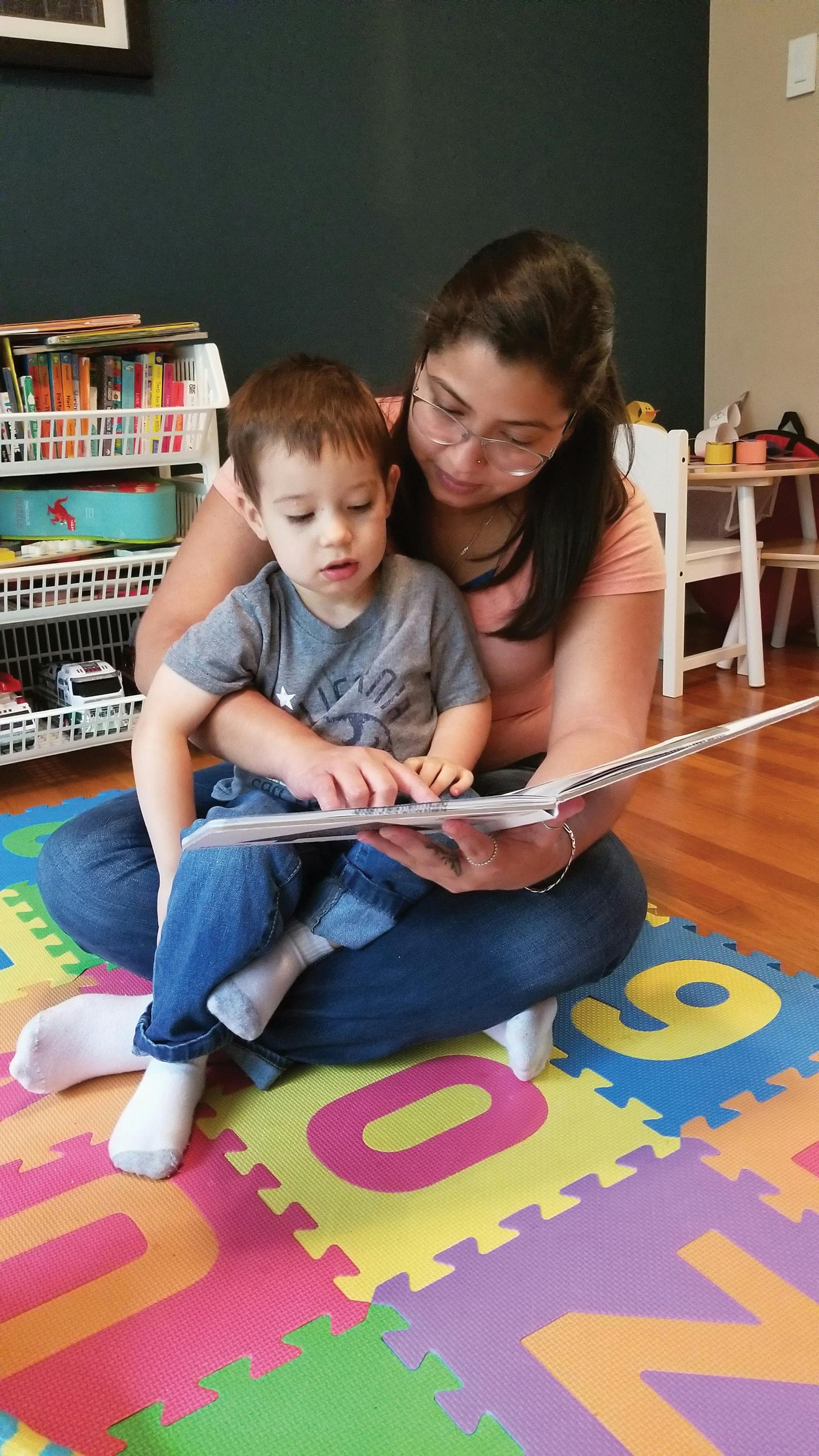 Person and child sitting on floor reading a book