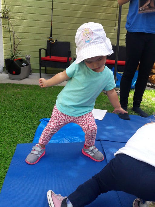 Child in a hat and patterned pants standing on a blue mat