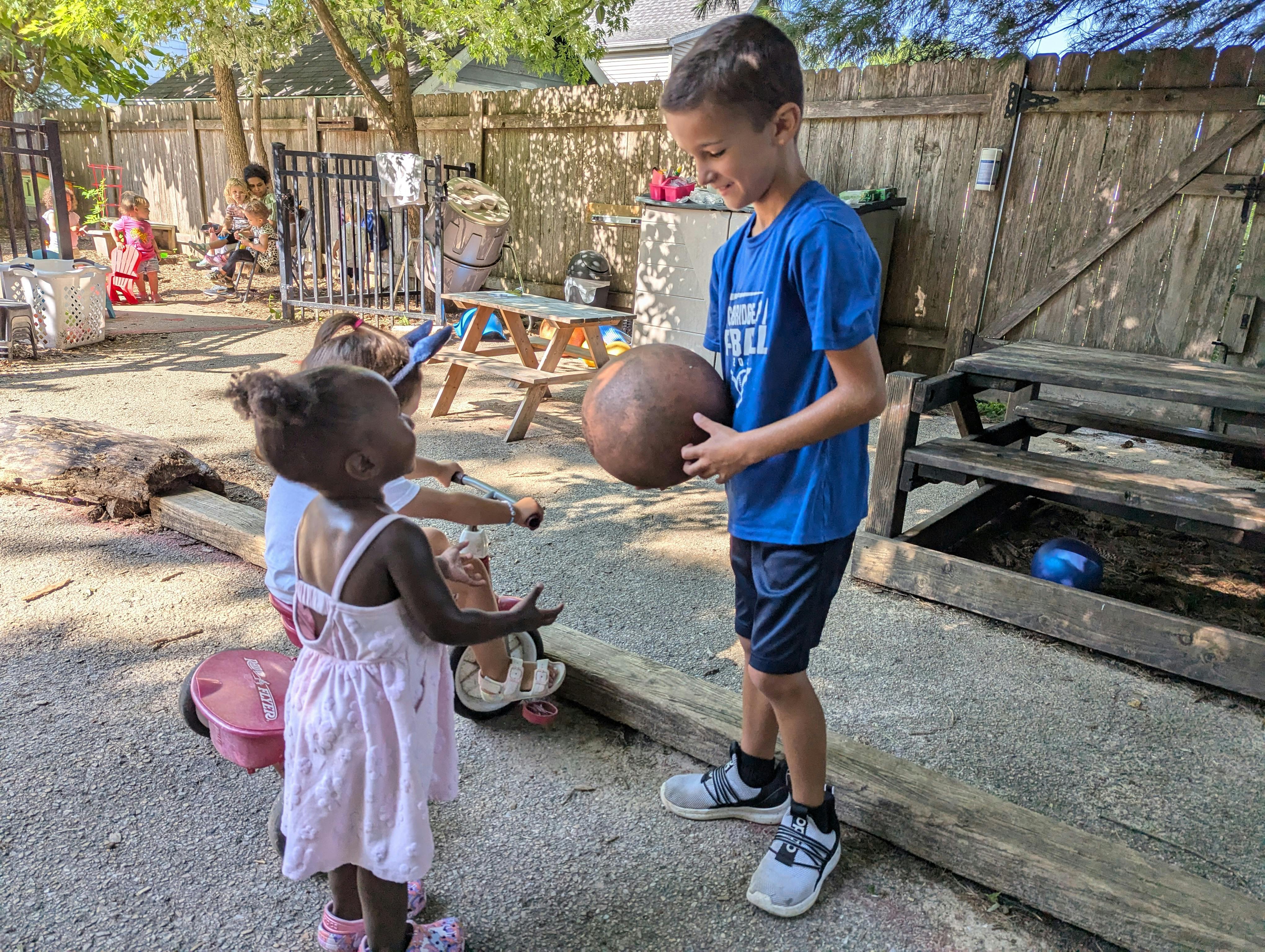 Child in blue shirt holding a ball, facing a child in a pink dress
