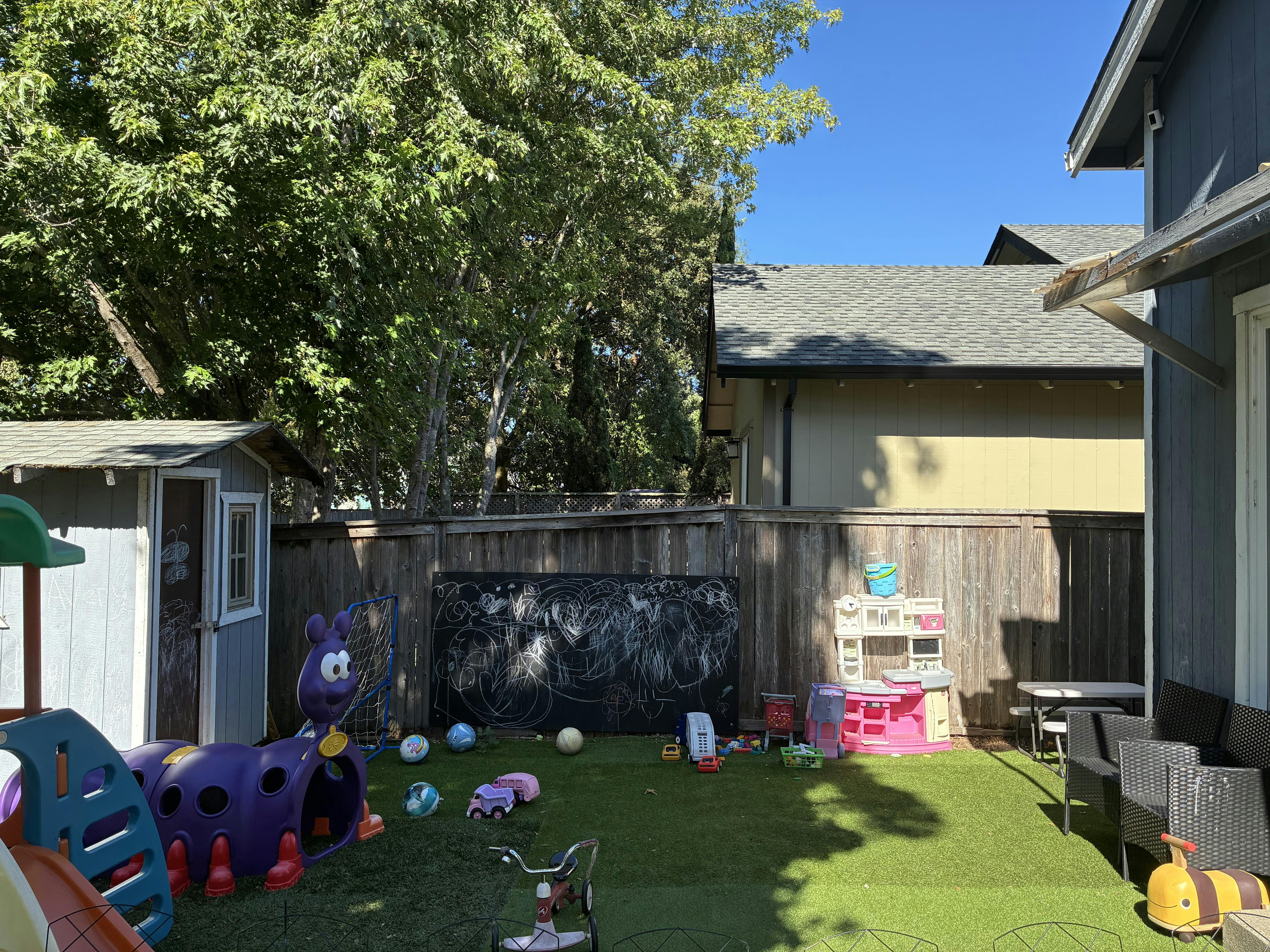 Backyard play area with toy structures, chalkboard, and lawn on a sunny day