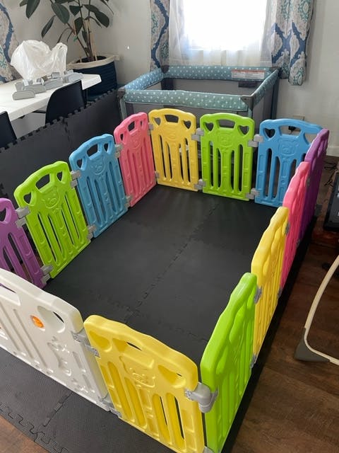 Colorful playpen on a black mat with a crib in the background