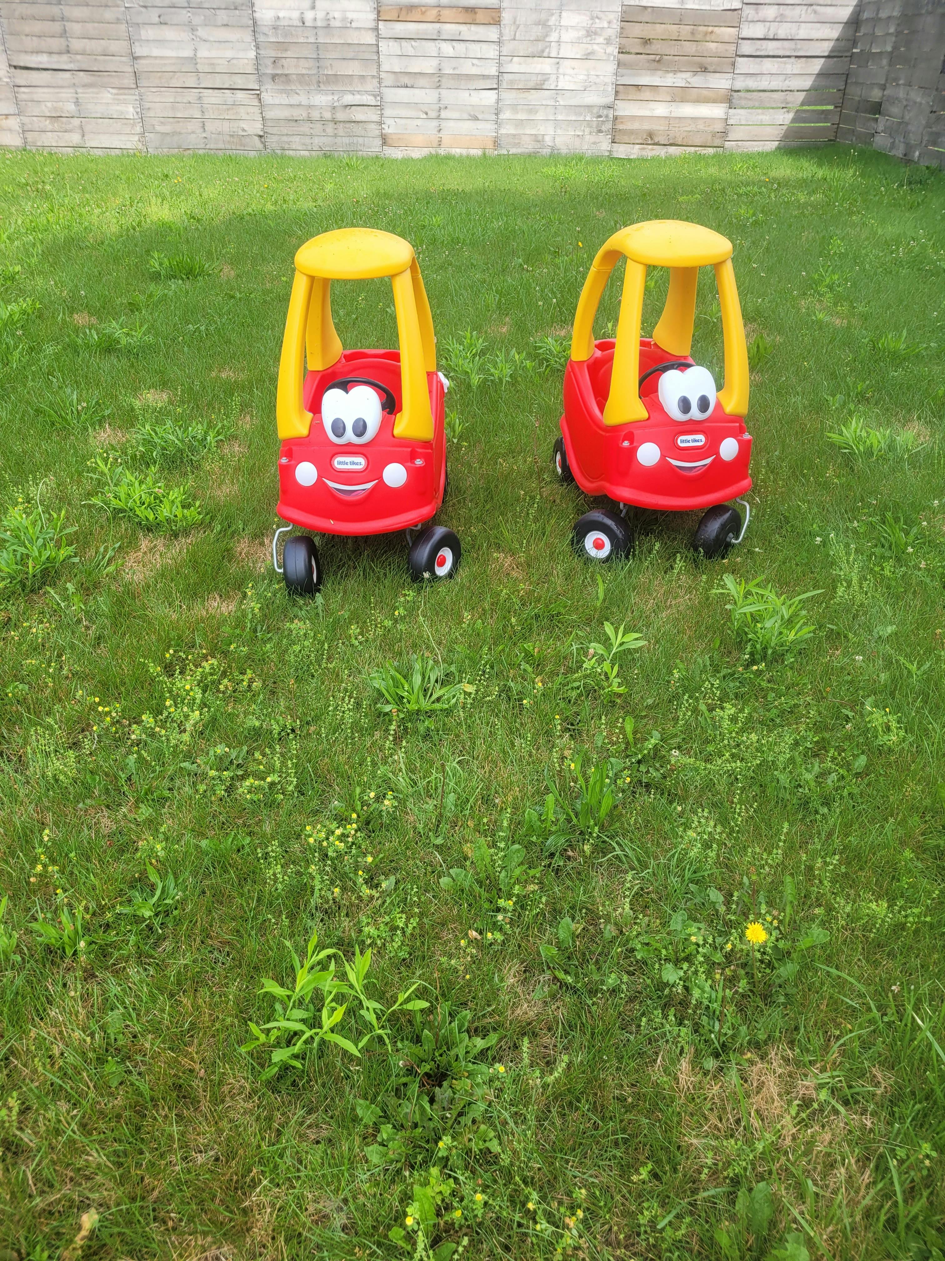 Two toy cars on green grass next to a wooden fence