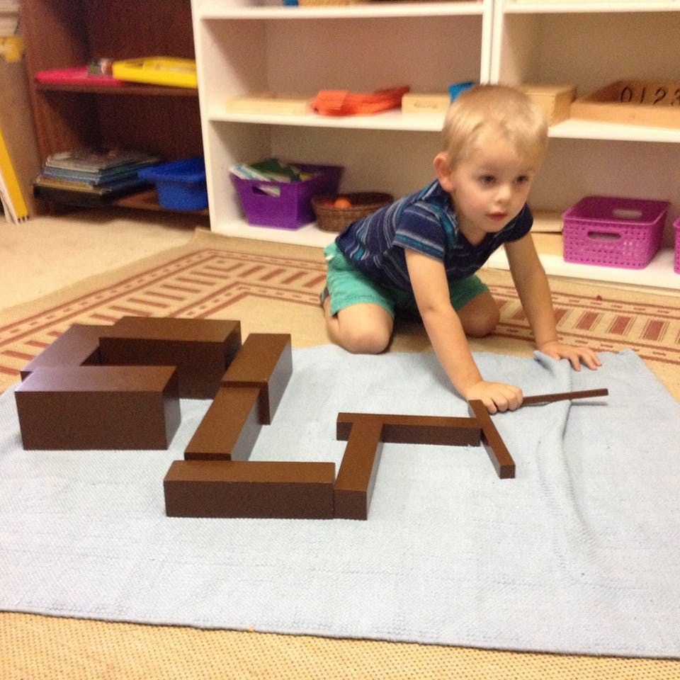 Child kneeling on floor playing with brown wooden blocks